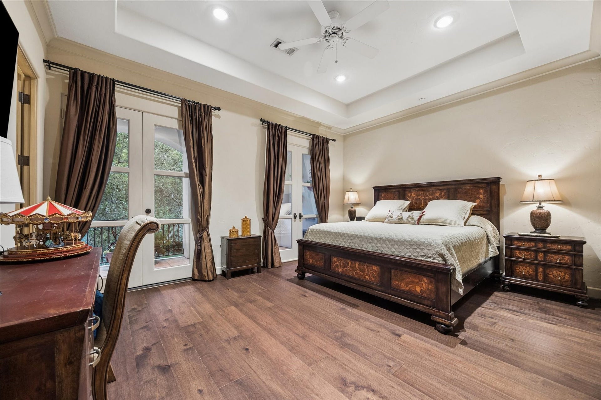 2 Lacewood Lane, Piney Point Village, TX 77024 Upstairs en-suite bedroom with tray ceiling detail, warm wood flooring, and private balcony access overlooking the grounds.