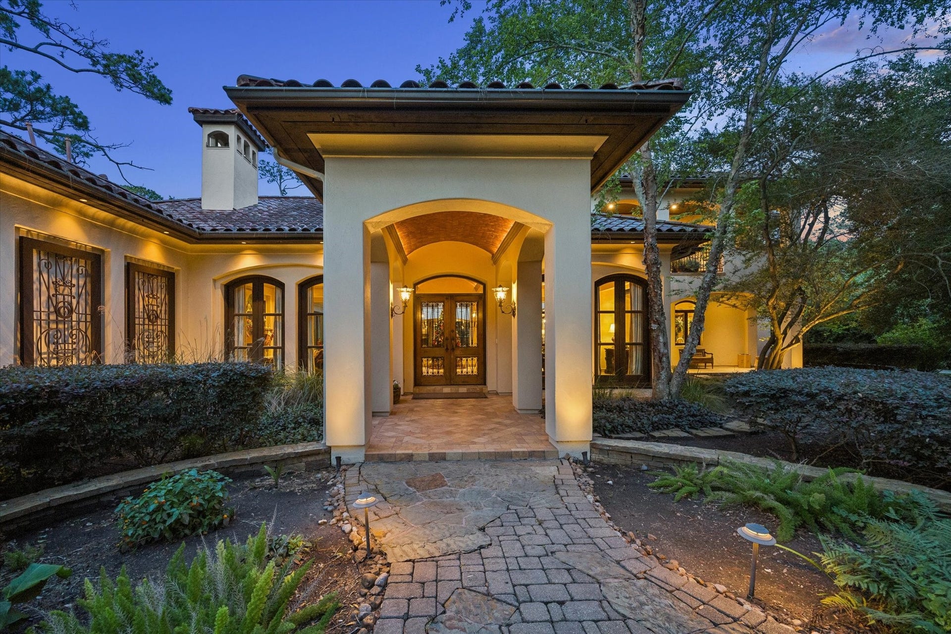 2 Lacewood Lane, Piney Point Village, TX 77024 Warm twilight entry showcasing Mediterranean architecture, arched details, and mature landscaping in a private Piney Point setting.