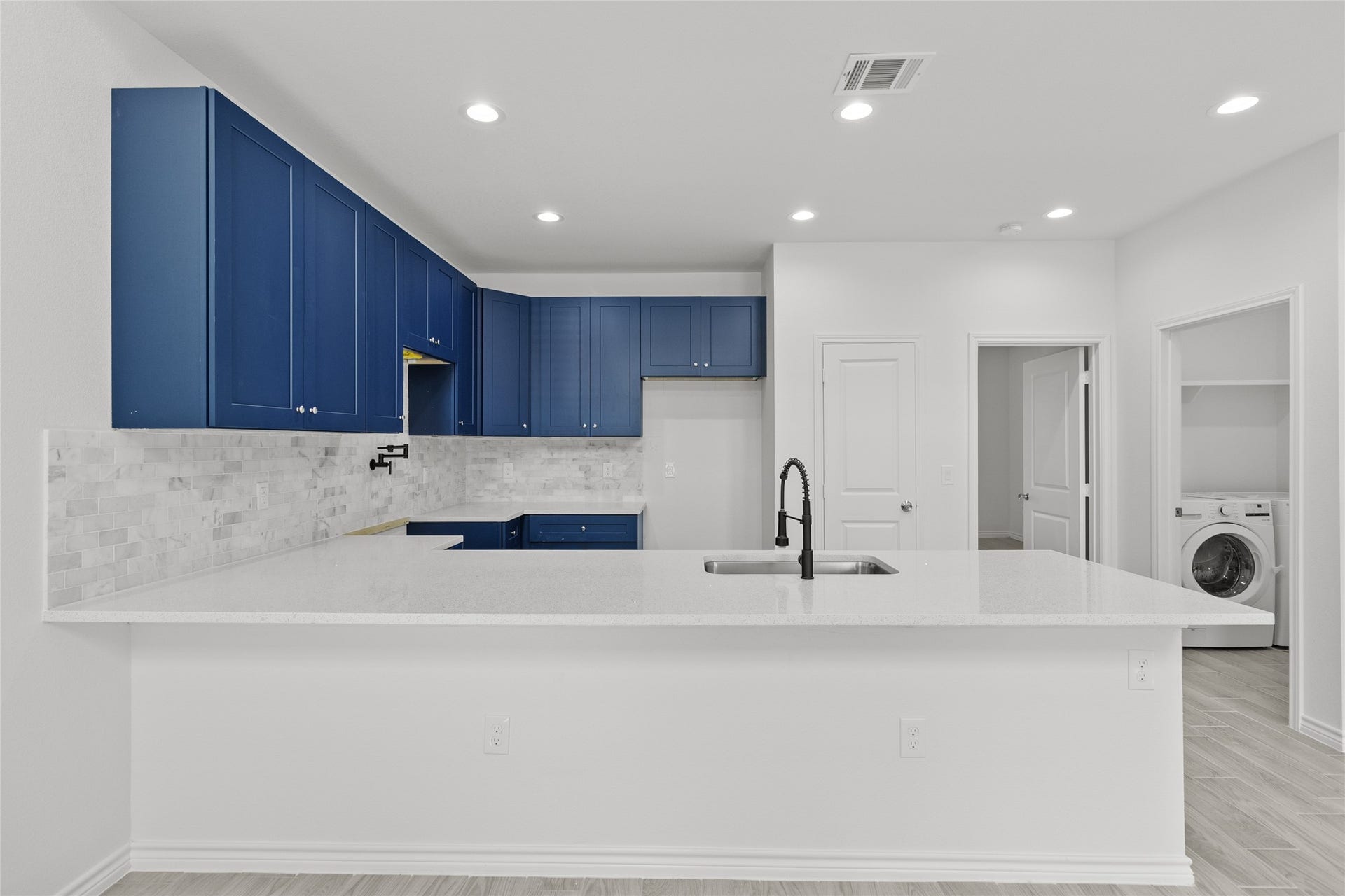760 Juneau Court, Montgomery, TX 77316 This is a modern kitchen with sleek blue cabinetry, white countertops, stainless steel appliances, and a laundry area to the side. It features an open layout and bright lighting.