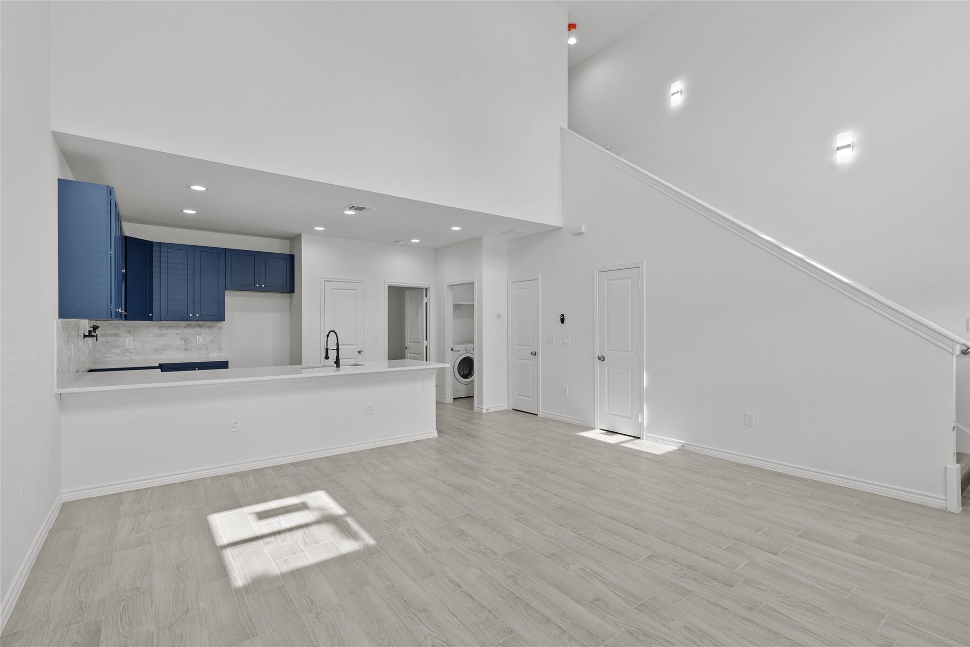760 Juneau Court, Montgomery, TX 77316 You're looking at a modern, open-concept space featuring a sleek kitchen with navy blue cabinets and stainless steel appliances, a bright living area with ample natural light, and a convenient laundry nook. The room boasts fresh white walls and light wood flooring, with a staircase leading to the upper level.