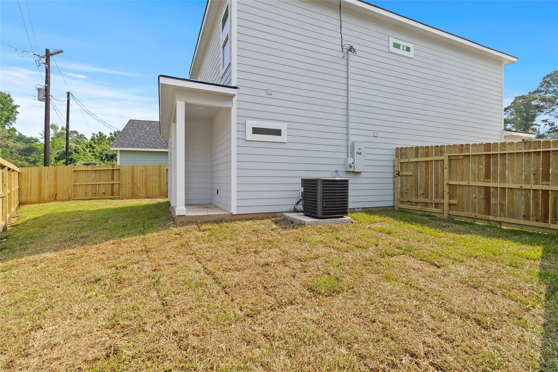 760 Juneau Court, Montgomery, TX 77316 This is a side yard of a modern two-story home featuring a well-maintained wooden fence, a small grassy lawn, central air conditioning unit, and a sheltered side entrance.