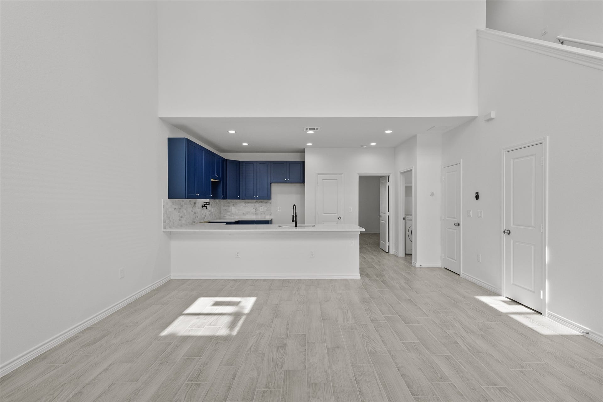 760 Juneau Court, Montgomery, TX 77316 This is a modern, open-concept interior featuring a spacious living area with light wood flooring and white walls. It includes a sleek kitchen with blue cabinetry and a breakfast bar. The layout offers multiple doors for room access and natural light streaming in.