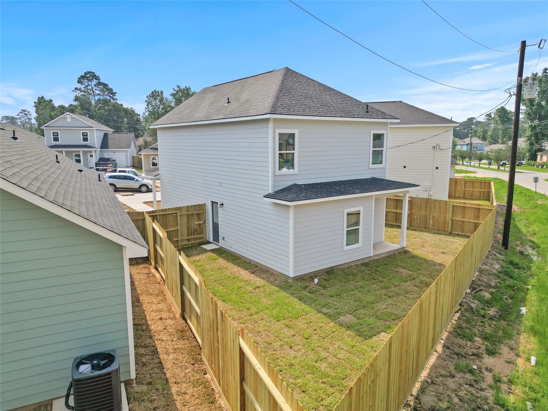 760 Juneau Court, Montgomery, TX 77316 This is an aerial shot of a two-story, detached house with a fresh, modern exterior, featuring a fenced backyard and a small attached deck. The neighborhood appears to be newly developed with similar style homes nearby.