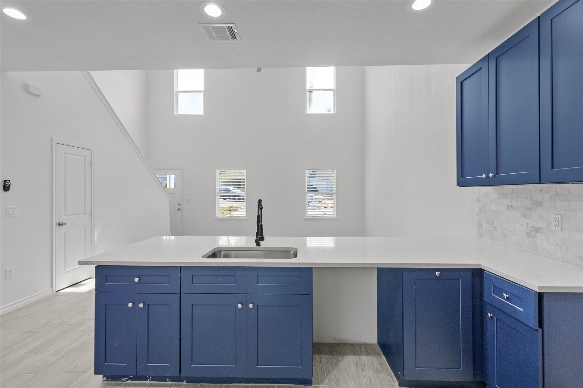 760 Juneau Court, Montgomery, TX 77316 This is a bright, modern kitchen with high ceilings, white walls, and sleek blue cabinetry. It features stainless steel appliances, a large central island with a sink, and a stylish subway tile backsplash. The space is well-lit with natural light from multiple windows and recessed ceiling lights.