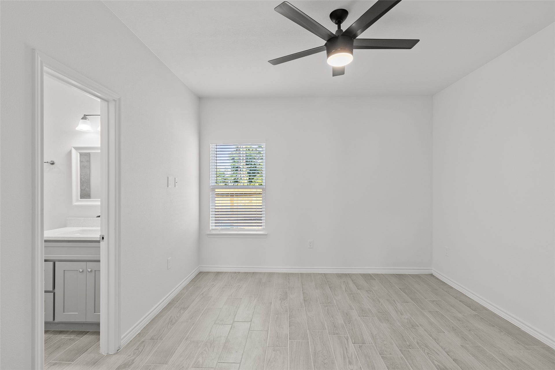 760 Juneau Court, Montgomery, TX 77316 This is a bright, modern room featuring fresh white walls, a ceiling fan with lighting, and wood-look flooring. There's a window for natural light and an en-suite bathroom visible.