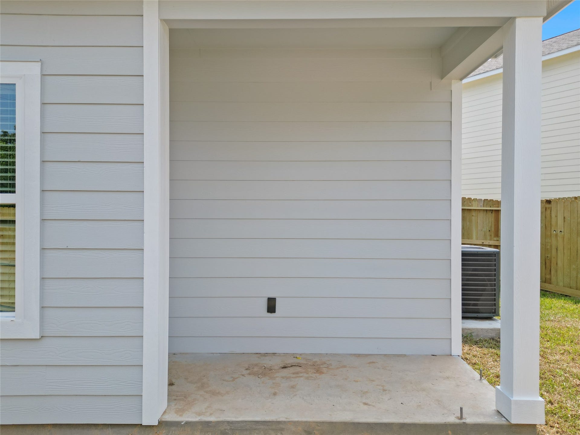 760 Juneau Court, Montgomery, TX 77316 This is a covered outdoor patio area with a concrete floor, part of a house with light-colored siding. It appears to be a small, cozy space for outdoor relaxation or dining, with a view of a fenced backyard.