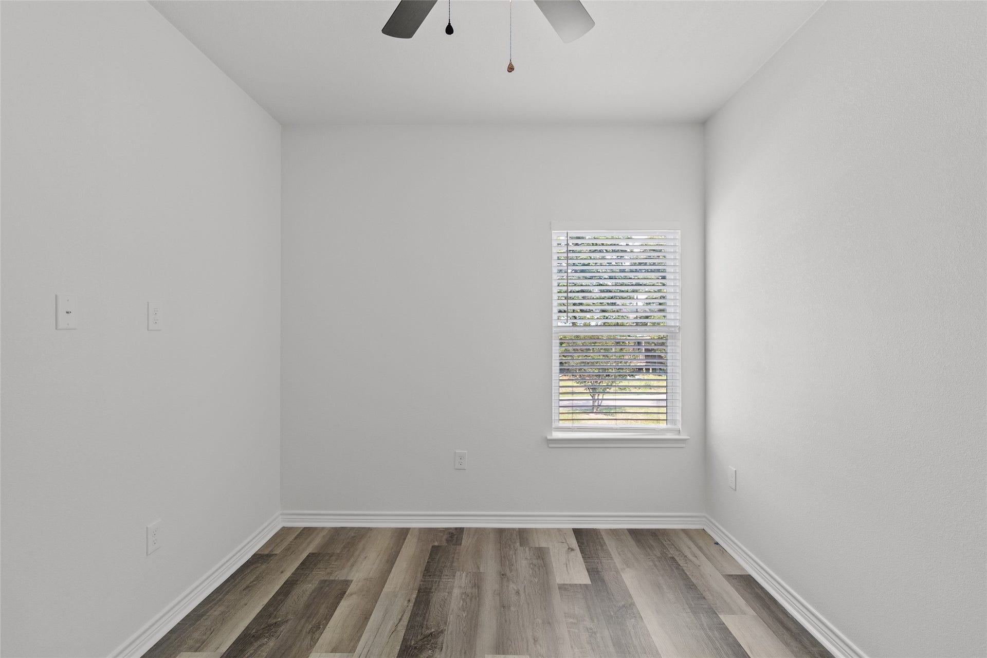 760 Juneau Court, Montgomery, TX 77316 This is a vacant room with fresh white walls, modern wood laminate flooring, a single window with blinds, and a ceiling fan with lighting. It offers a clean canvas for personalization.