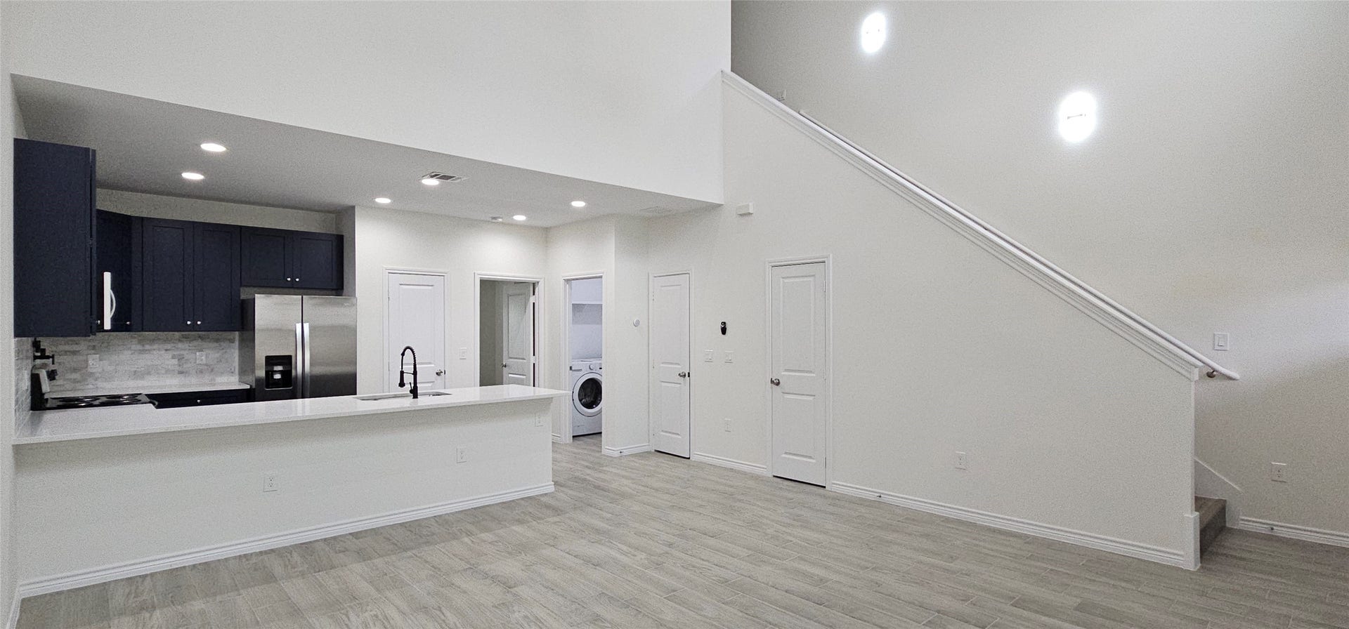760 Juneau Court, Montgomery, TX 77316 This is a modern, open-plan space featuring a sleek kitchen with dark cabinetry and stainless steel appliances, a breakfast bar, and a bright living area with wood flooring. There's also a convenient laundry nook and access to a staircase leading to another level.