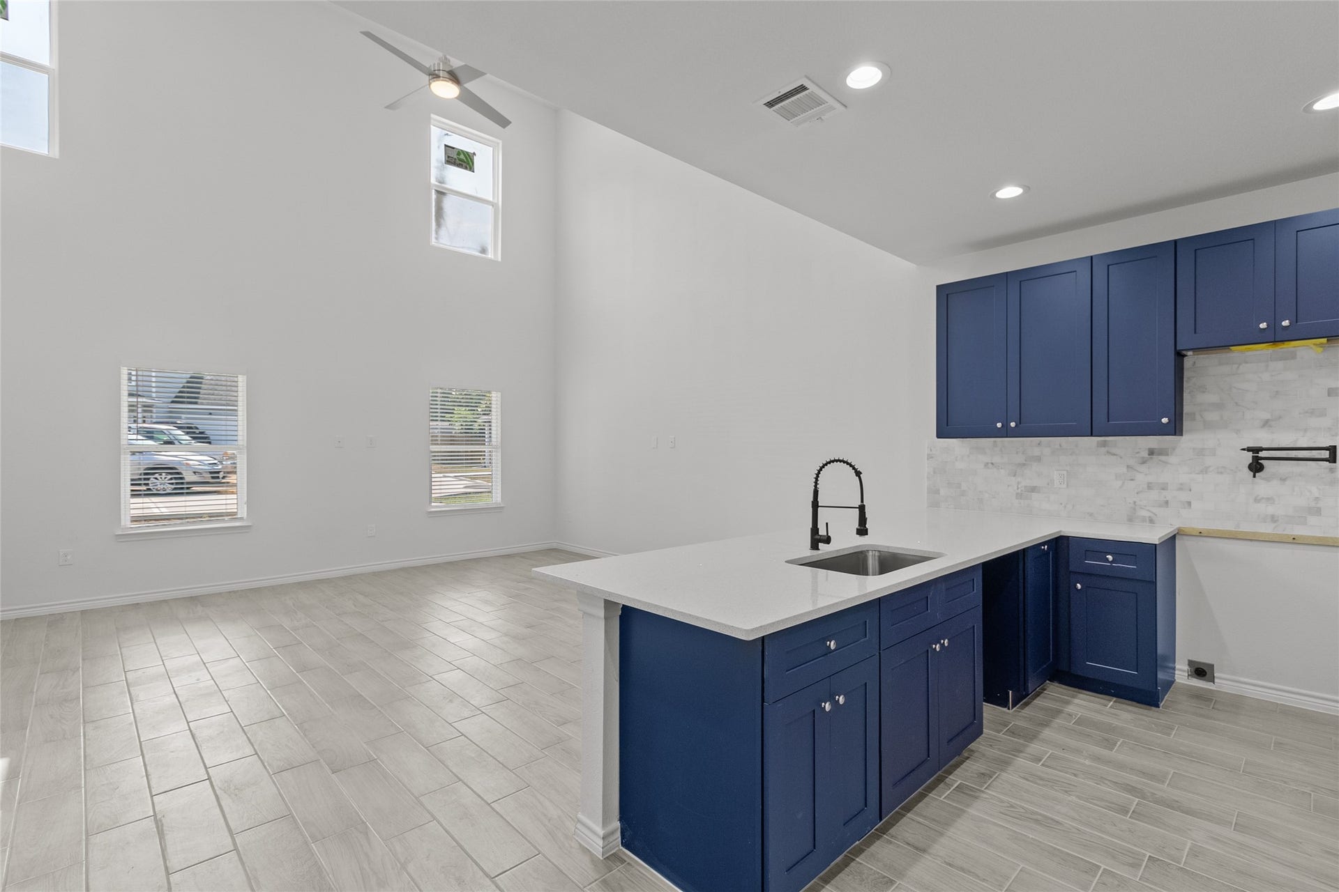760 Juneau Court, Montgomery, TX 77316 This is a modern kitchen with high ceilings, sleek blue cabinetry, white countertops, and stainless steel fixtures. There's ample natural light from multiple windows, and the space features tile flooring.