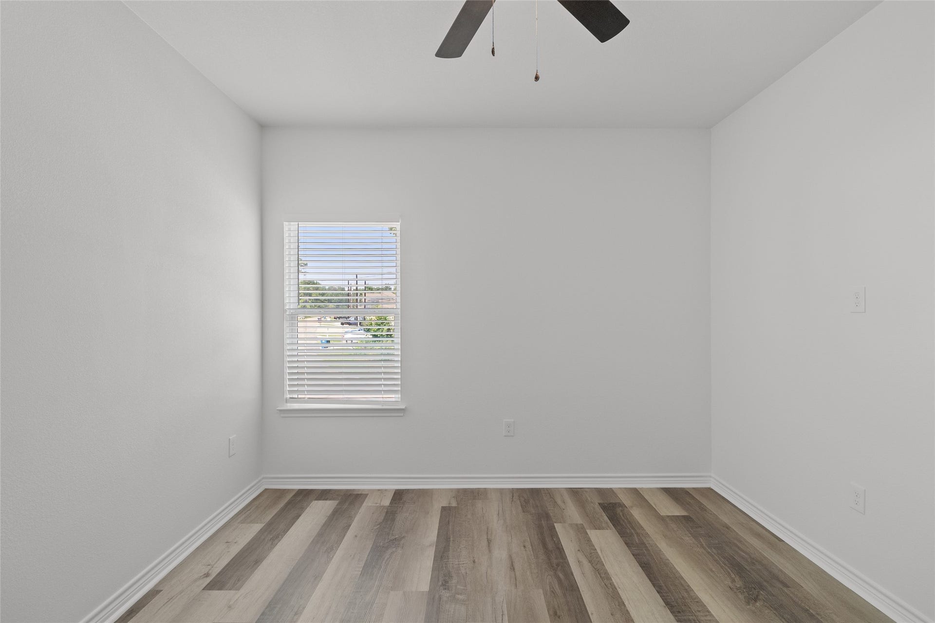 760 Juneau Court, Montgomery, TX 77316 This is a bright, unfurnished room featuring a high ceiling with a ceiling fan, a large window with horizontal blinds, and modern wood-look flooring.