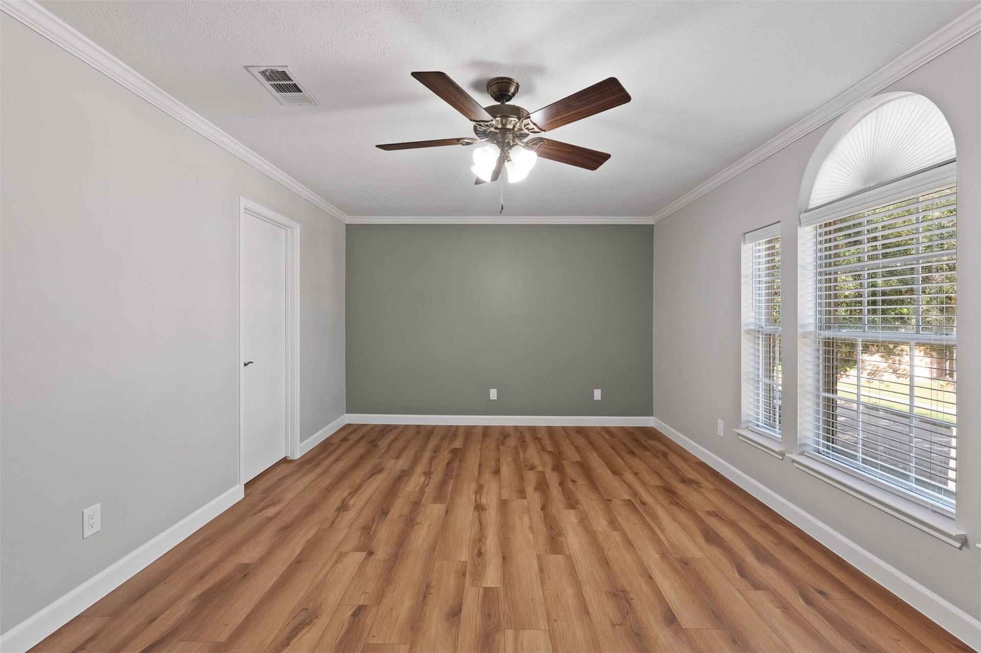 1118 Wentworth Drive, Pearland, TX 77584 A sage green accent wall complements the warm wood-look flooring and crisp crown molding in this secondary bedroom. Wide windows topped with a decorative arch bring in abundant light, while a dark wood ceiling fan adds style and breeze.