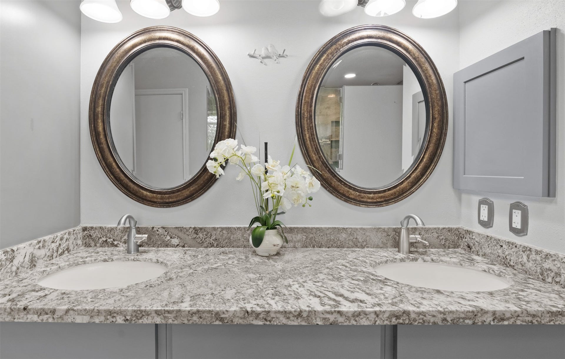 1118 Wentworth Drive, Pearland, TX 77584 Renovated vanity with granite countertops features a dual sink layout with brushed nickel faucets and oval mirrors. Custom grey wall-mounted storage and updated vanity lighting complete this spa-inspired space.