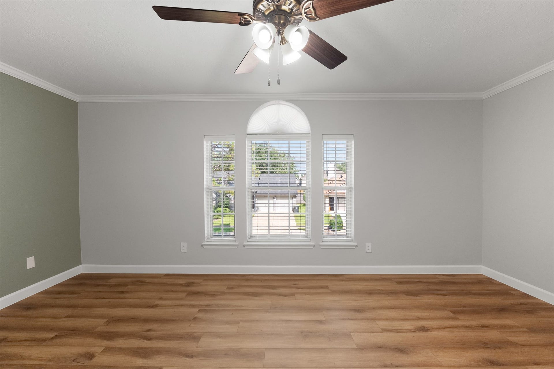 1118 Wentworth Drive, Pearland, TX 77584 An arched center window framed by classic blinds serves as the focal point of this secondary bedroom, filling the room with light. Fresh neutral paint, crown molding, a sage green accent wall, and warm wood-look flooring combine to create a versatile space.