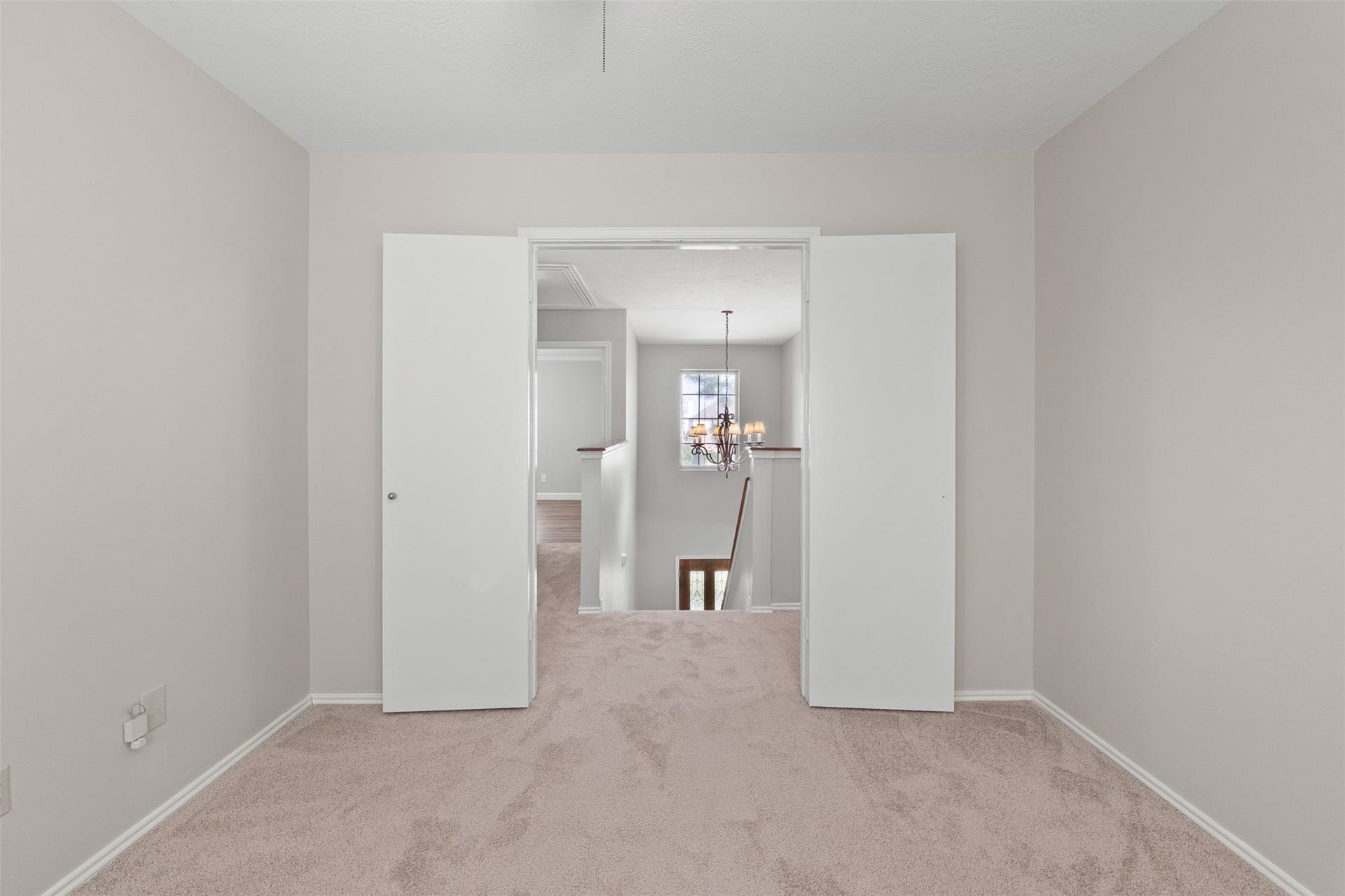 1118 Wentworth Drive, Pearland, TX 77584 Double doors open to reveal this versatile secondary bedroom featuring fresh interior paint, soft carpet flooring, and a clear view out toward the upper landing chandelier.