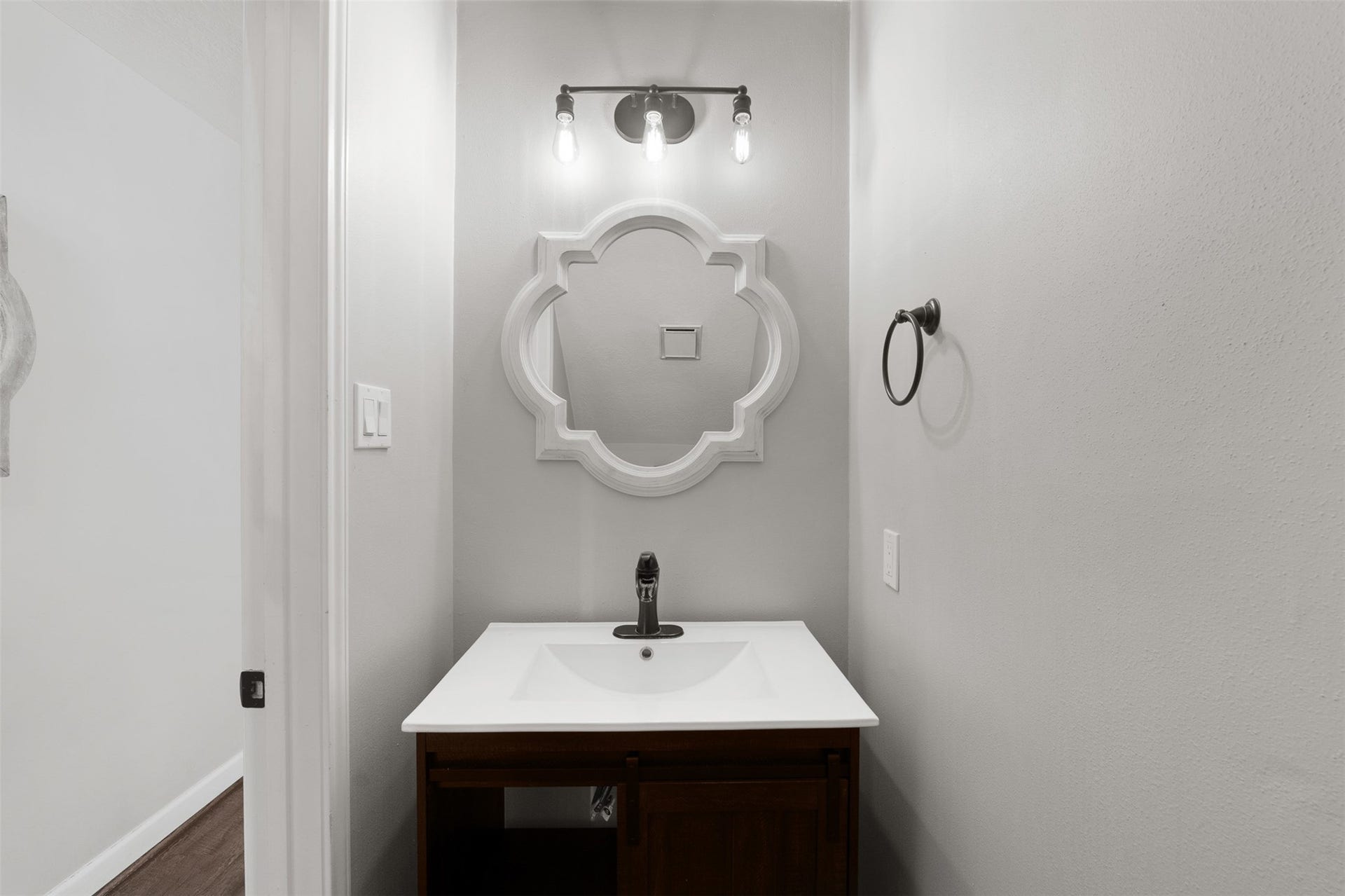 1118 Wentworth Drive, Pearland, TX 77584 Featuring a renovated vanity with a white countertop and dark wood cabinetry, this half bath boasts a white quatrefoli mirror and vintage-inspired three-light sconce. Modern dark hardware and neutral walls create a polished, functional space for guests.