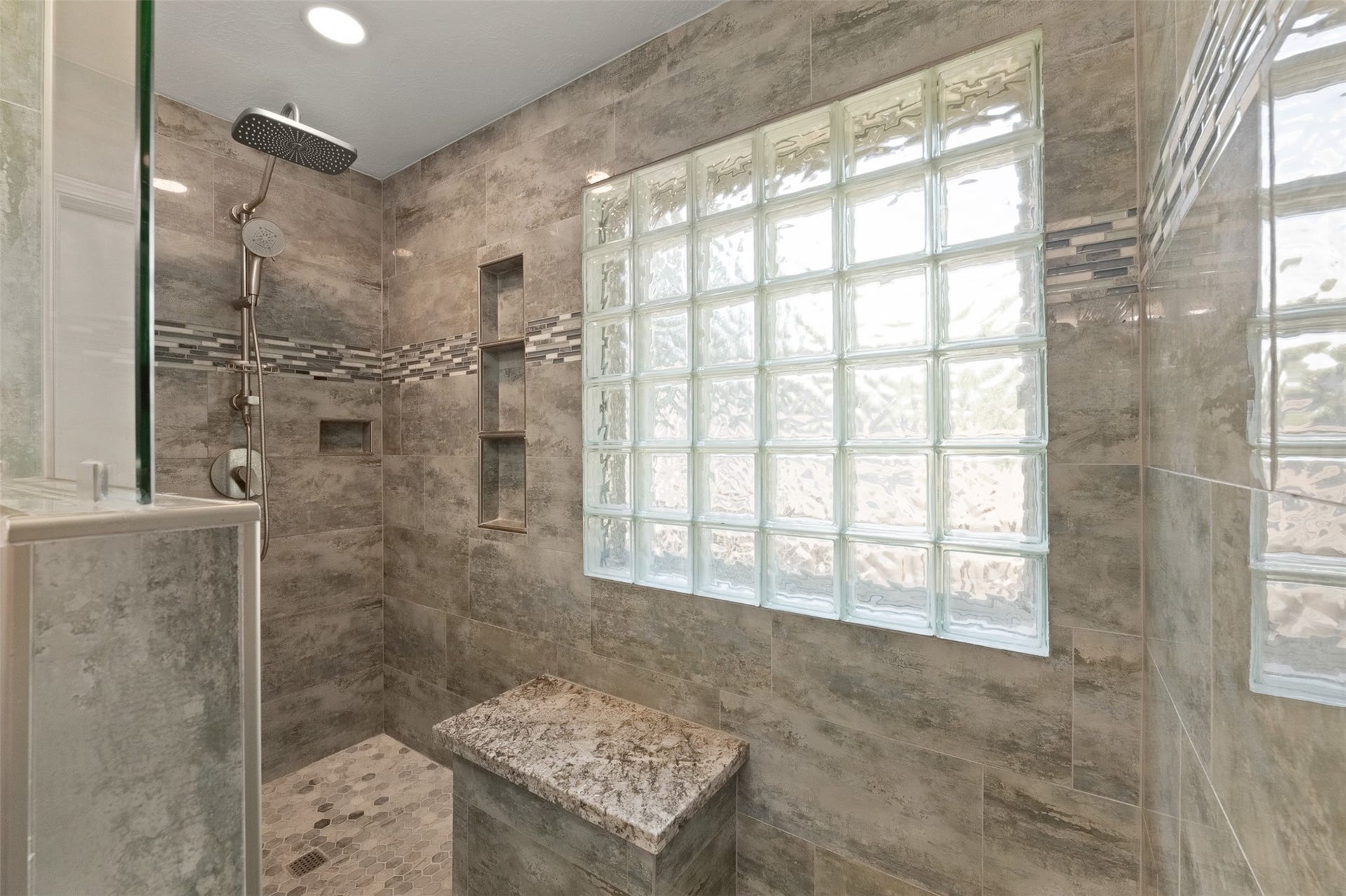 1118 Wentworth Drive, Pearland, TX 77584 Framed in large-format grey tile, this renovated walk-in shower features a rain shower head, built-in bench with granite top, and an inset storage niche. Glass block window provides soft natural light while maintaining complete privacy.