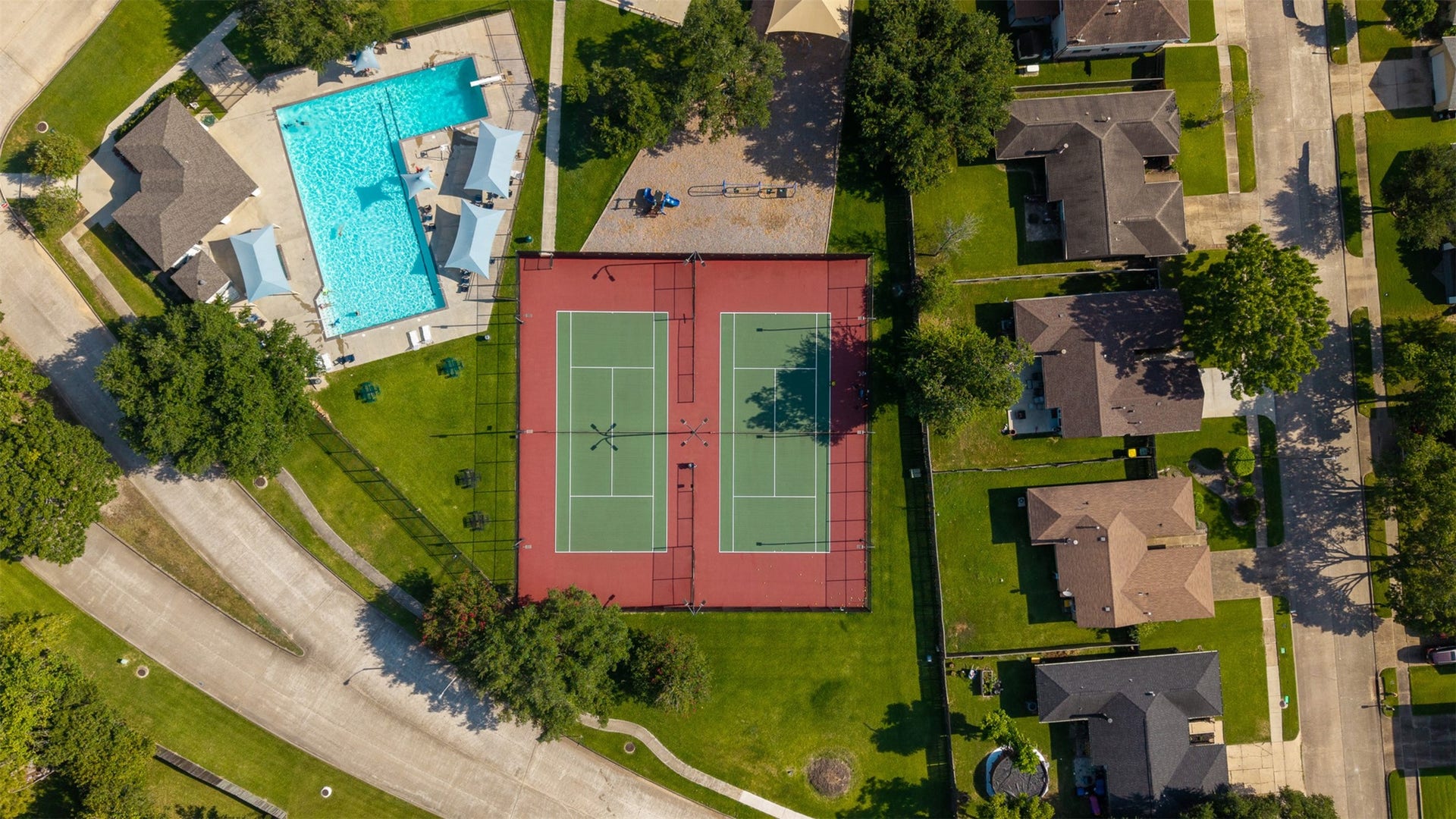 1118 Wentworth Drive, Pearland, TX 77584 High-angle aerial perspective reveals the neighborhood amenity center, featuring a shimmering community pool and tennis courts.