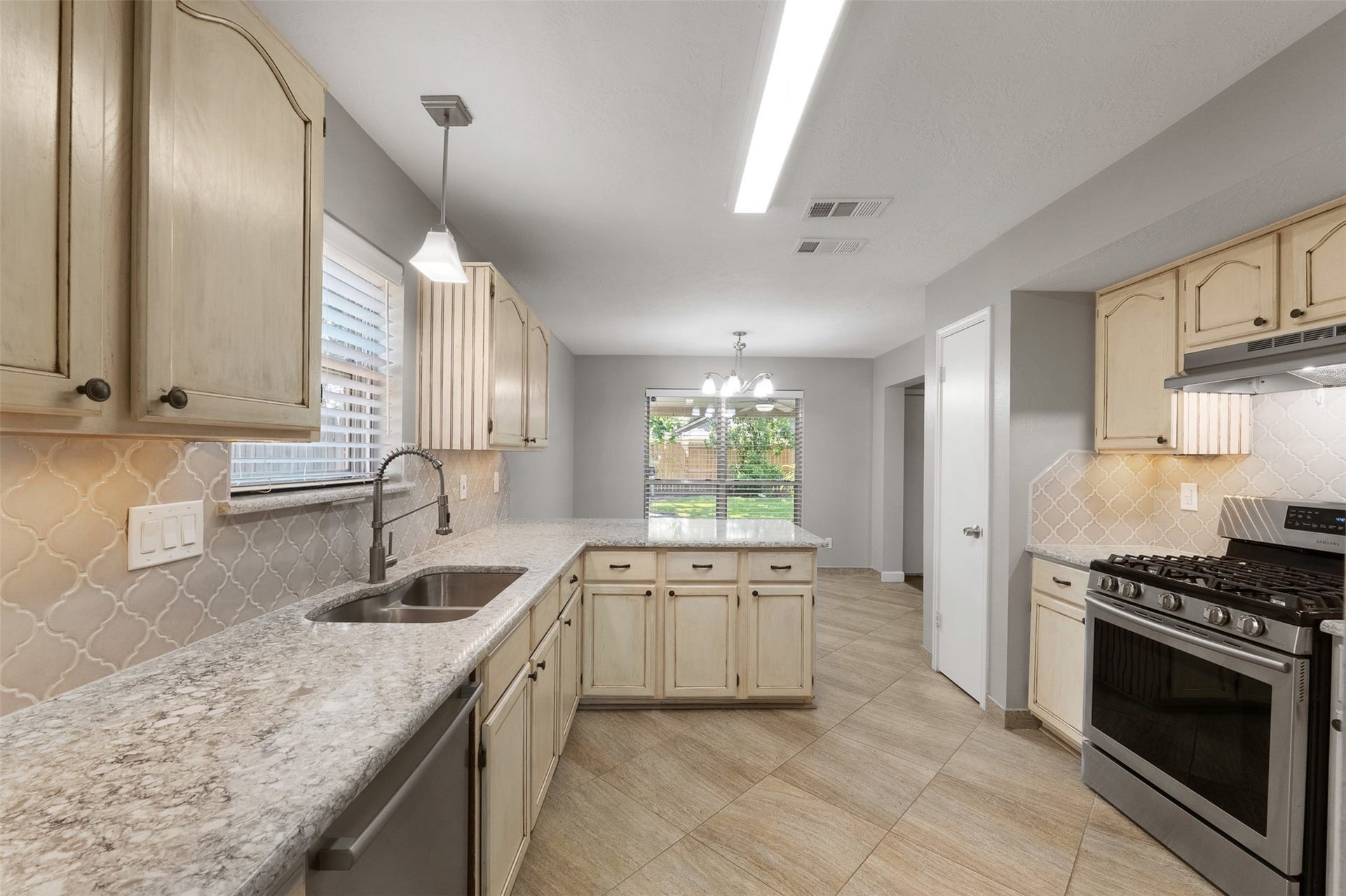 1118 Wentworth Drive, Pearland, TX 77584 Featuring quartz countertops and a designer backsplash, this kitchen showcases a gas cooktop, dual sink, and cream cabinetry with ample storage. The functional peninsula extends into a breakfast bar, seamlessly connecting to the sunlit breakfast area framed by oversized windows.