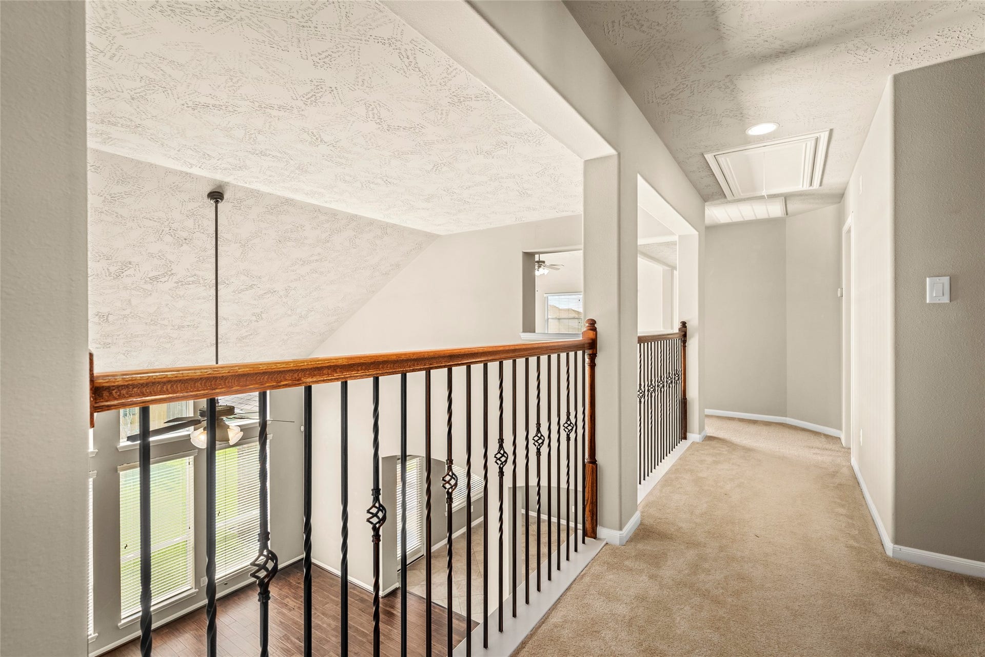 5307 Amber Sky Lane, Rosharon, TX 77583 This showcases the bright, open hallway with a modern metal and wood railing overlooking a two-story living area. The space features neutral carpeting and textured ceilings, creating a warm and inviting atmosphere. GOING TO THE GAME ROOM AND ROOMS