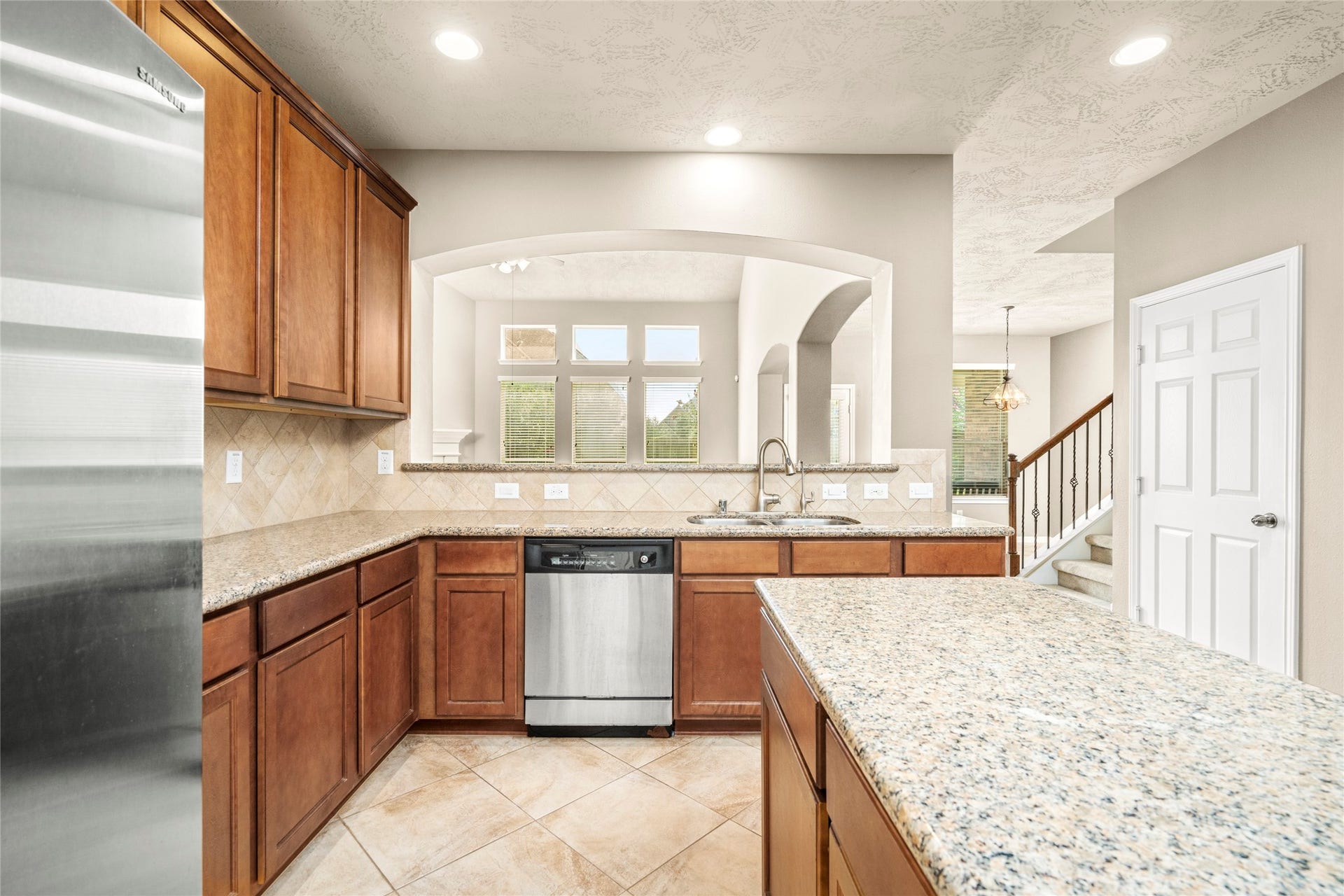 5307 Amber Sky Lane, Rosharon, TX 77583 This kitchen features granite countertops, wooden cabinetry, and stainless steel appliances. It opens to a bright living area with large windows and an arched pass-through, enhancing the spacious feel.