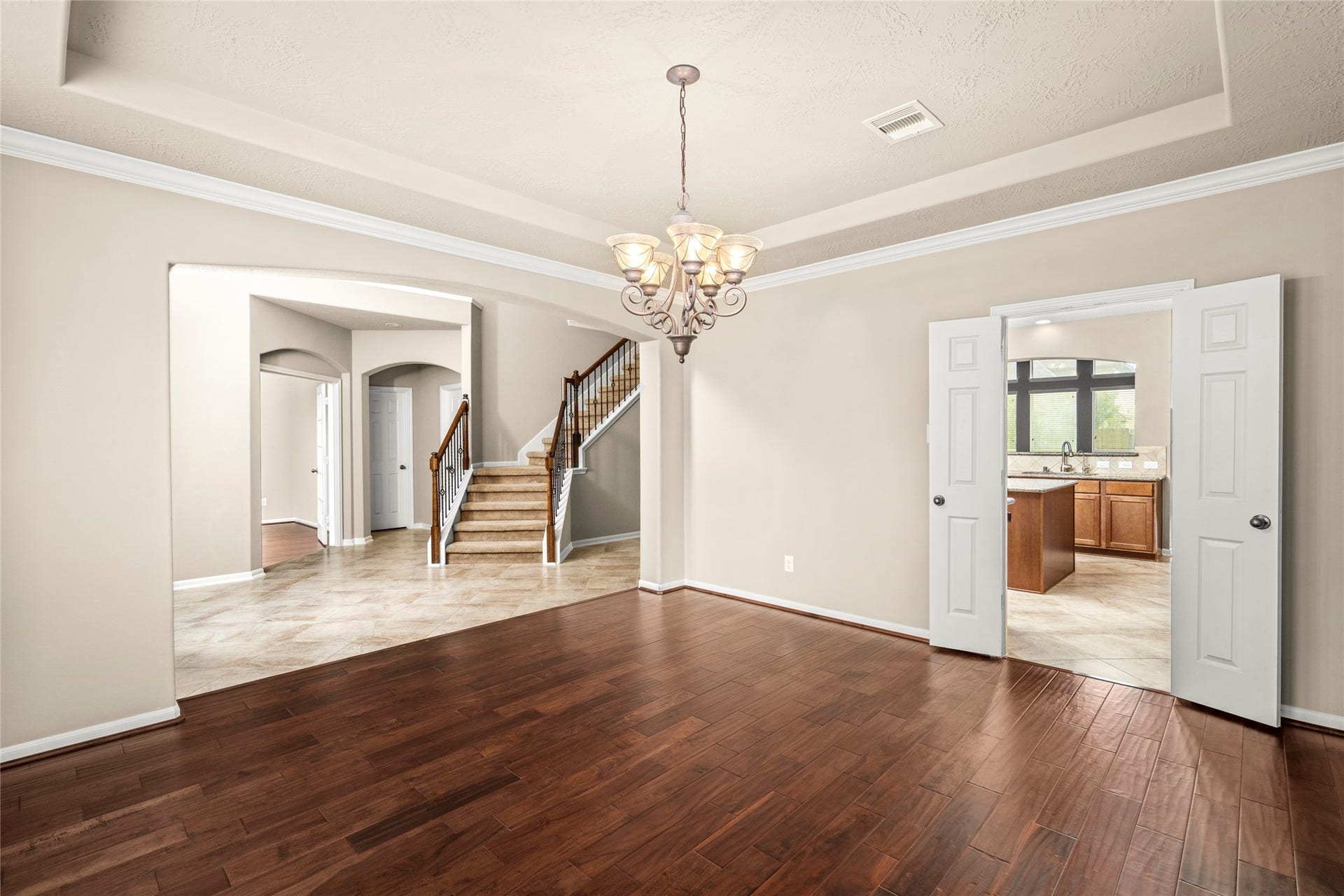 5307 Amber Sky Lane, Rosharon, TX 77583 A seamless transition of rich wood and tile flooring leads from the dining room toward the staircase and kitchen, illuminated by a striking chandelier. Luxury living, beautifully connected.