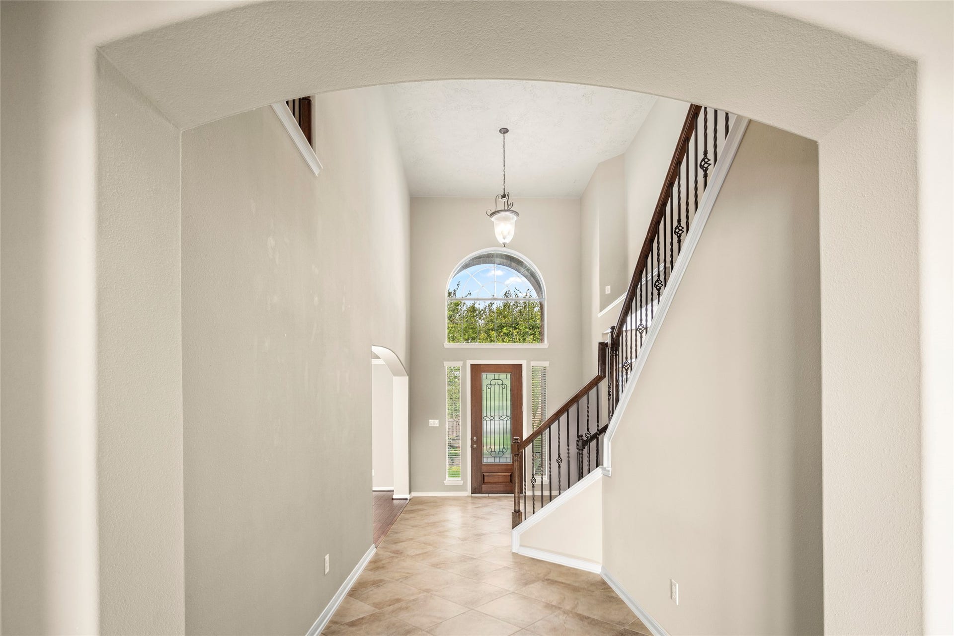 5307 Amber Sky Lane, Rosharon, TX 77583 Step into pure elegance: a dramatic two-story foyer crowned by a sweeping arched window, anchored by a graceful staircase finished in rich dark wood and wrought iron, set atop sun-kissed tile flooring.