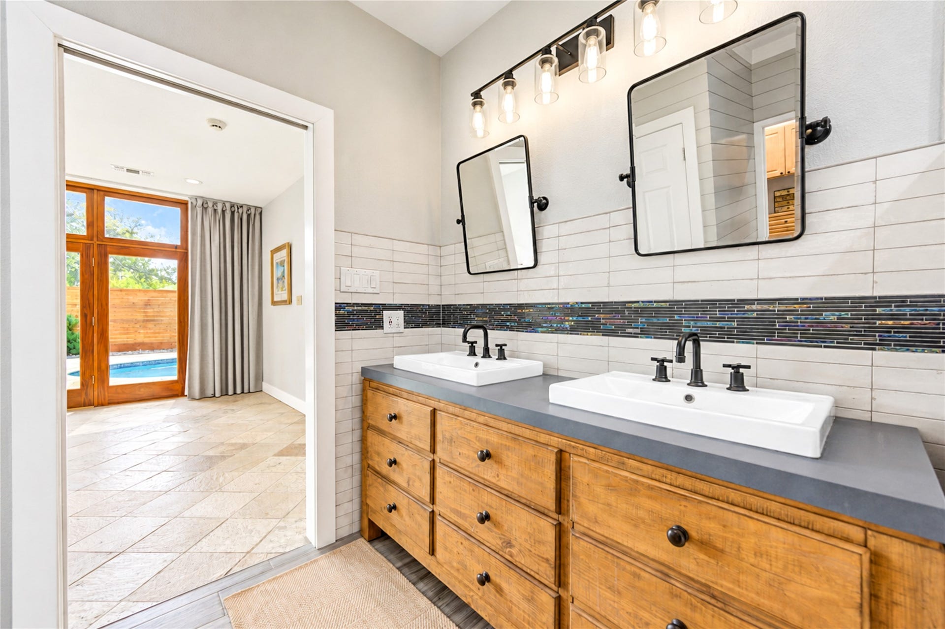 6211 Grovewood Lane, Houston, TX 77008 Linear white tile, a mosaic accent band and warm wood cabinetry frame the primary bath, with a view through to the glass doors of the primary bedroom.