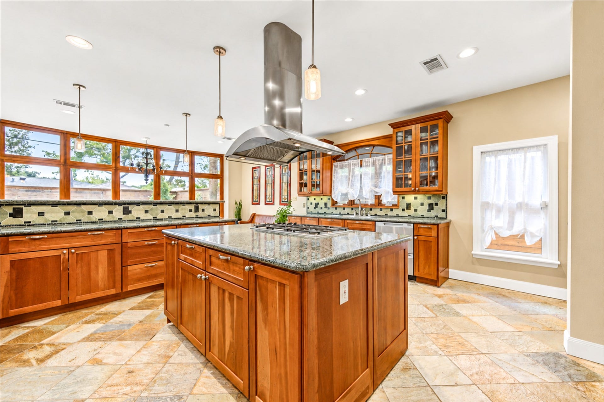 6211 Grovewood Lane, Houston, TX 77008 A gas cooktop island beneath the stainless vent hood anchors the kitchen, framed by a window wall and a decorative tile backsplash.
