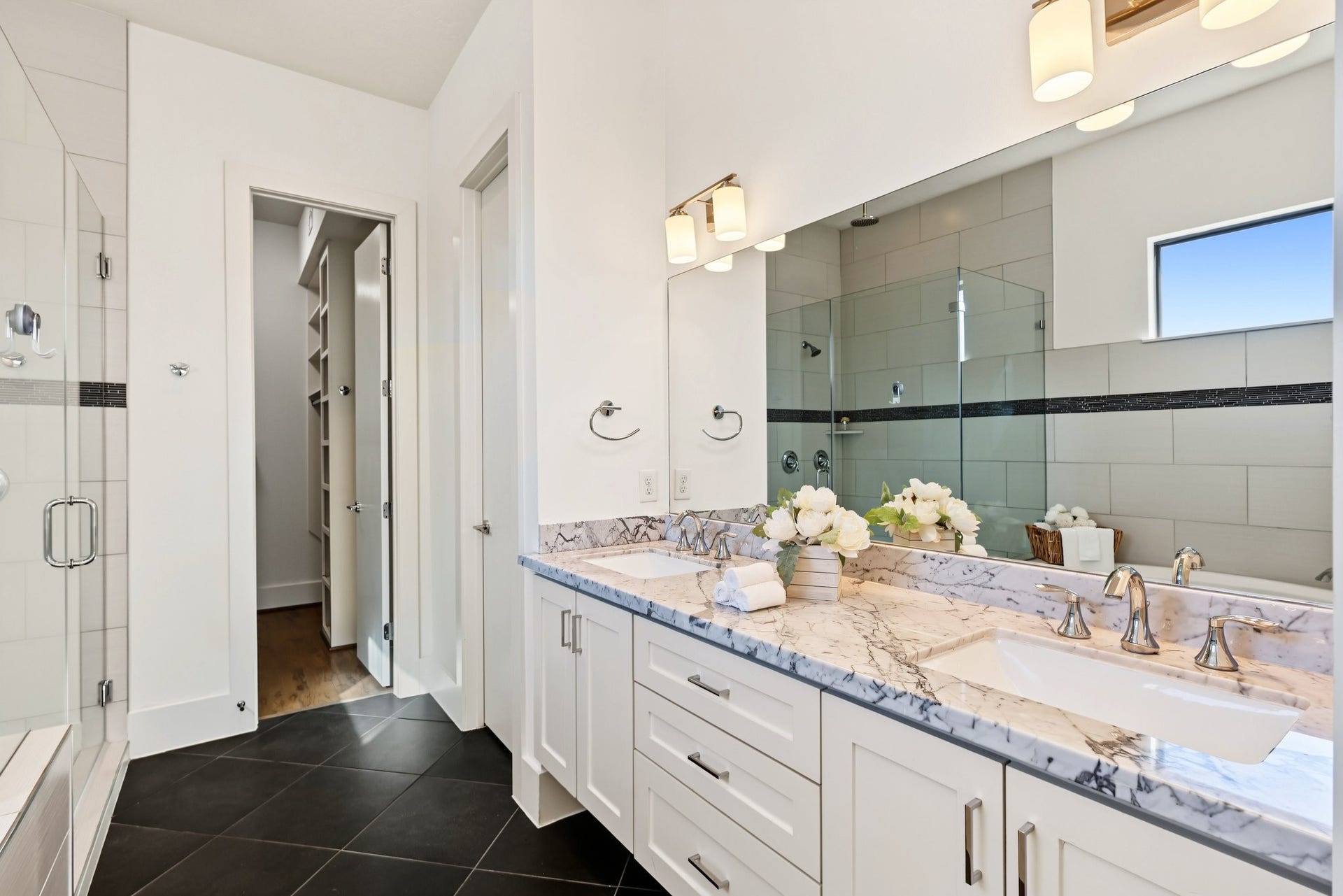 Choose between an invigorating rinse or a leisurely soak in the six-foot oval tub. A sleek, frameless glass shower enclosure featuring dual fixturesboth a wall-mounted head and an overhead rain showerelevates the daily routine into a spa-like ritual.