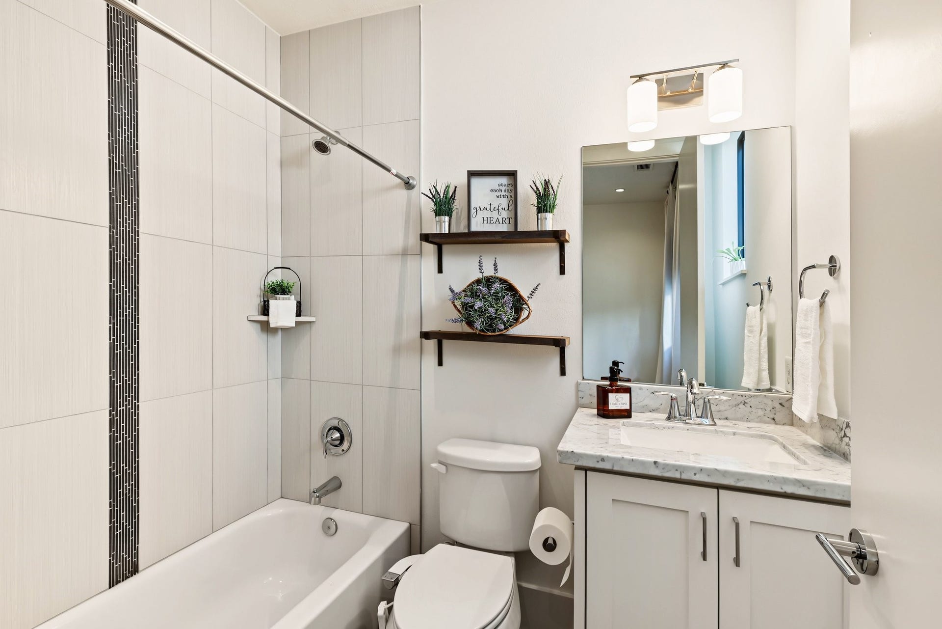 Unwind in a private en-suite bath where a deep soaking tub and full-height tile surround create a tranquil, spa-like setting. A contrasting dark mosaic accent adds tailored definition, while polished chrome fixtures complete the sleek, contemporary aesthetic.