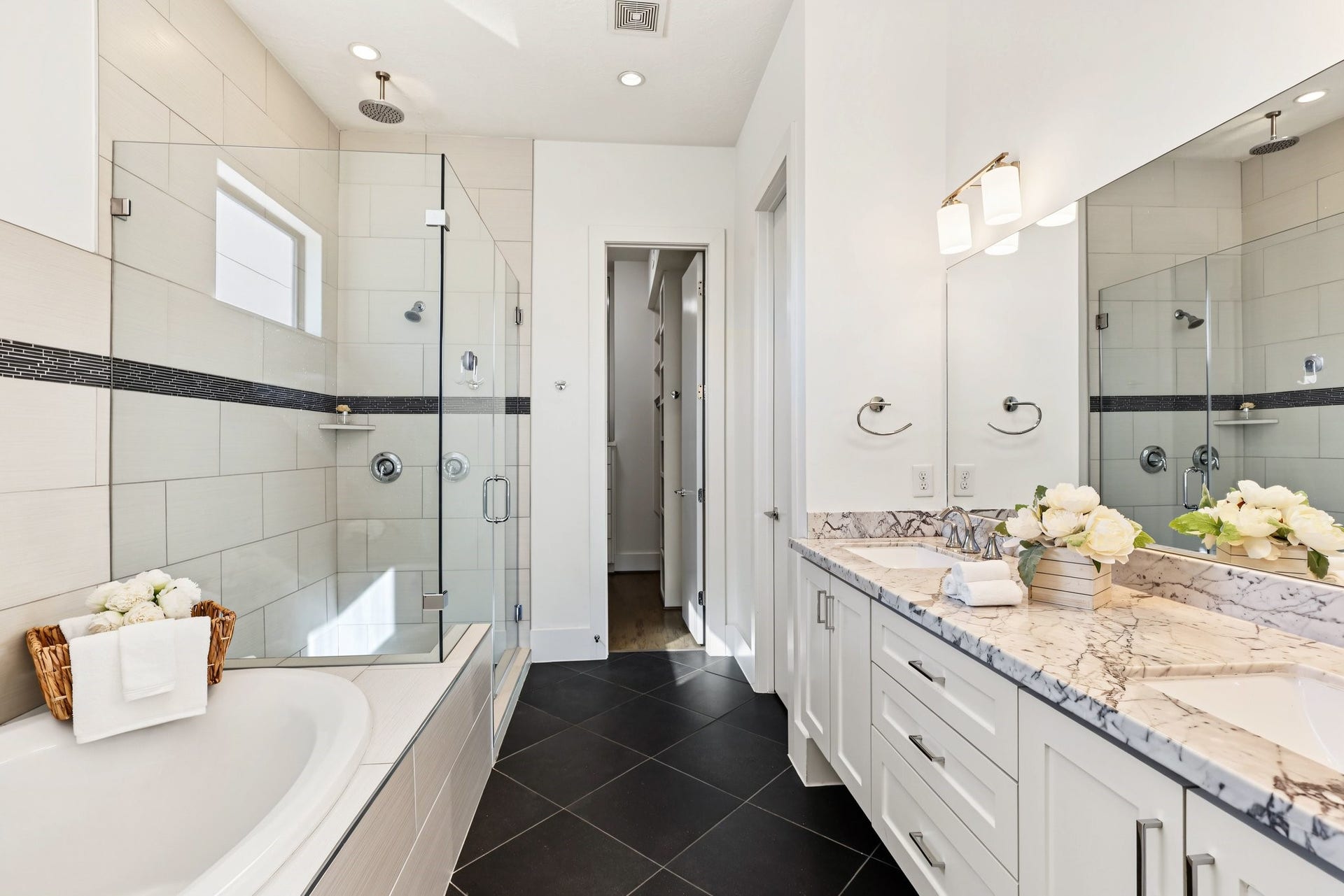 Begin and end each day in a serene primary bath tailored for unhurried routines. Honed marble countertops, dual undermount sinks, and a separate soaking tub and walk-in shower marry everyday convenience with a spa-like retreat. An overhead rainfall showerhead provides a refreshing daily indulgence, while classic Shaker-style cabinetry and clean-lined millwork complete the polished modern design.