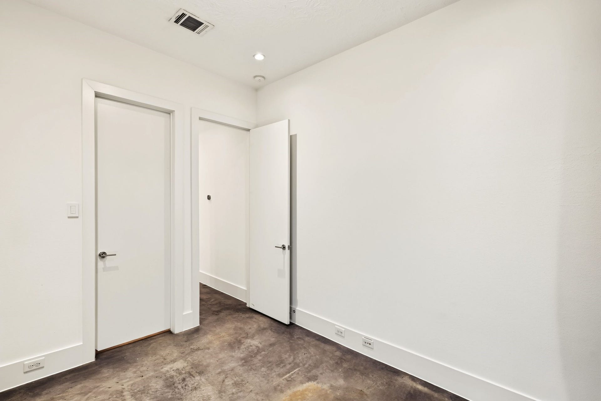Sealed, polished concrete floors lend sleek, low-maintenance modern flair to this versatile ground-level space. High ceilings, crisp white walls, and recessed LED lighting establish an airy, bright retreat tailored for a quiet guest suite or an executive home office.