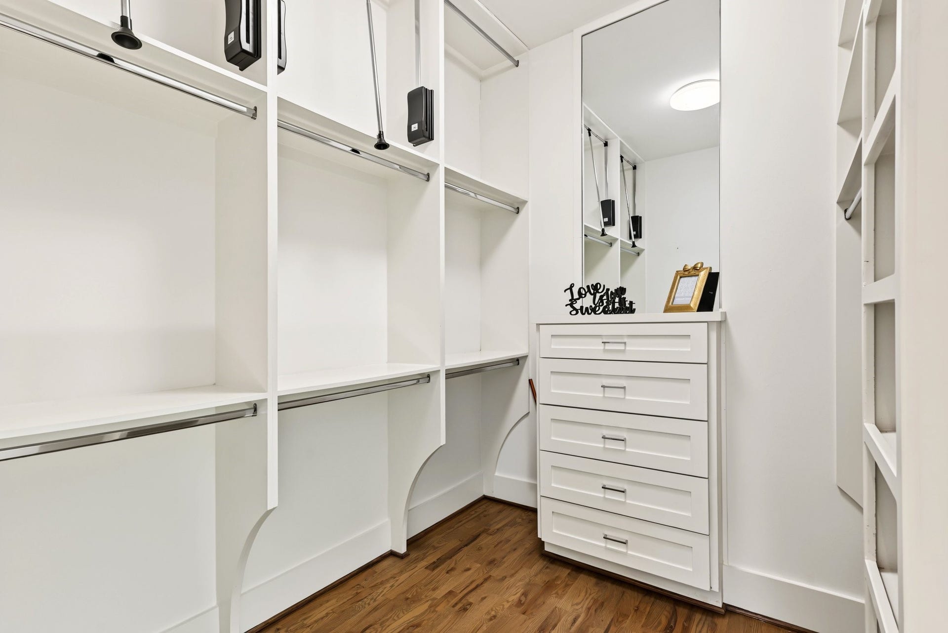 Bring boutique-style organization home in this expansive primary walk-in closet. Tailored with custom white built-ins, abundant open shelving, and multi-tier hanging rodscomplete with pull-down upper railsthe space maximizes vertical storage for a meticulously curated wardrobe of clothing, footwear, and accessories.