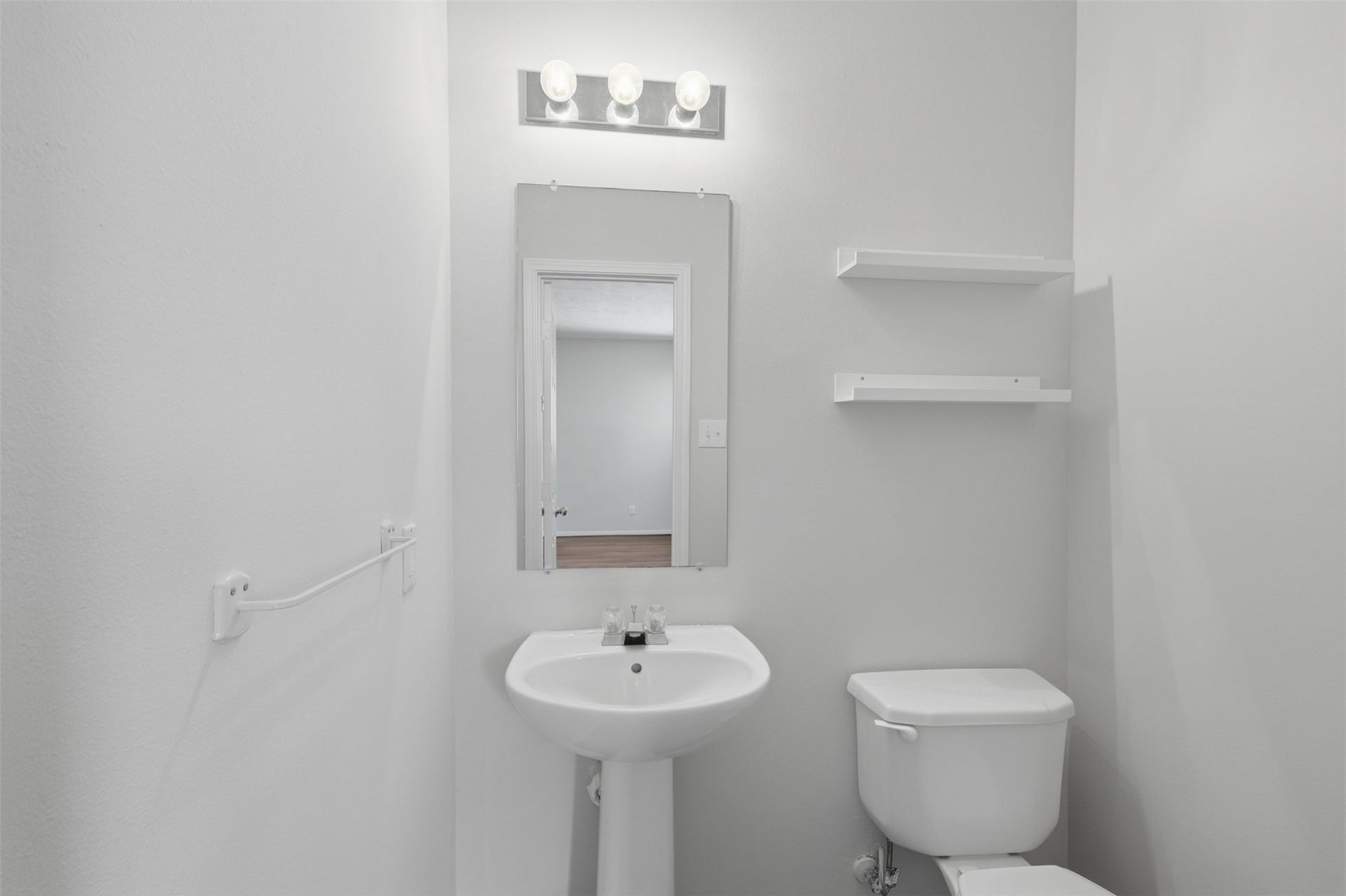 Convenient first-floor half bath located just off the main living areas, freshly painted and featuring a pedestal sink and decorative mirror.
