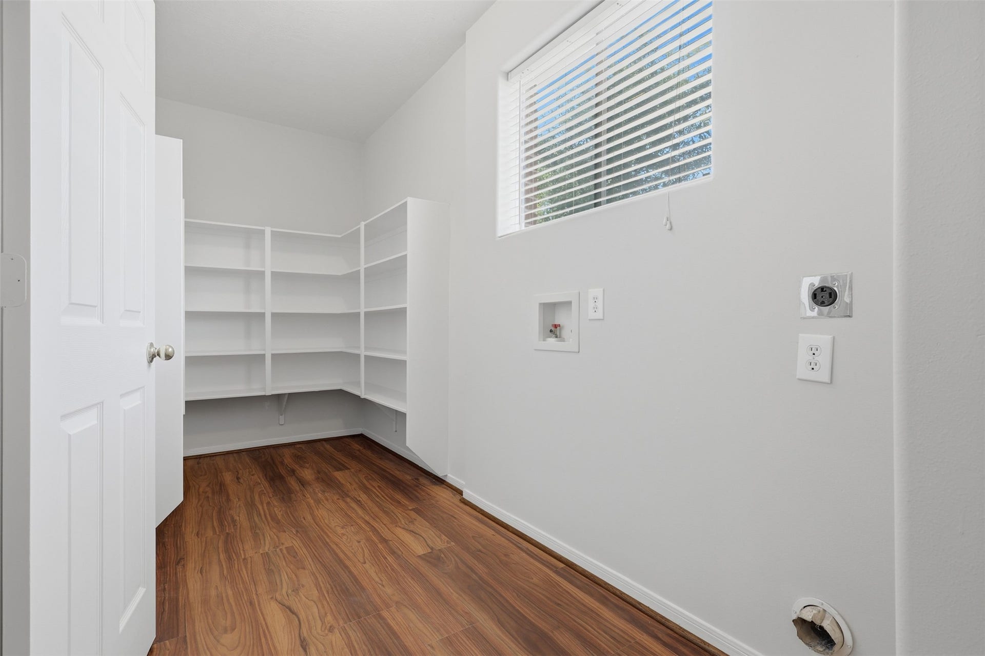 Spacious pantry and utility room featuring built-in shelving for organized storage, utility hookups, a window for natural light, and durable brand new LVP flooring.