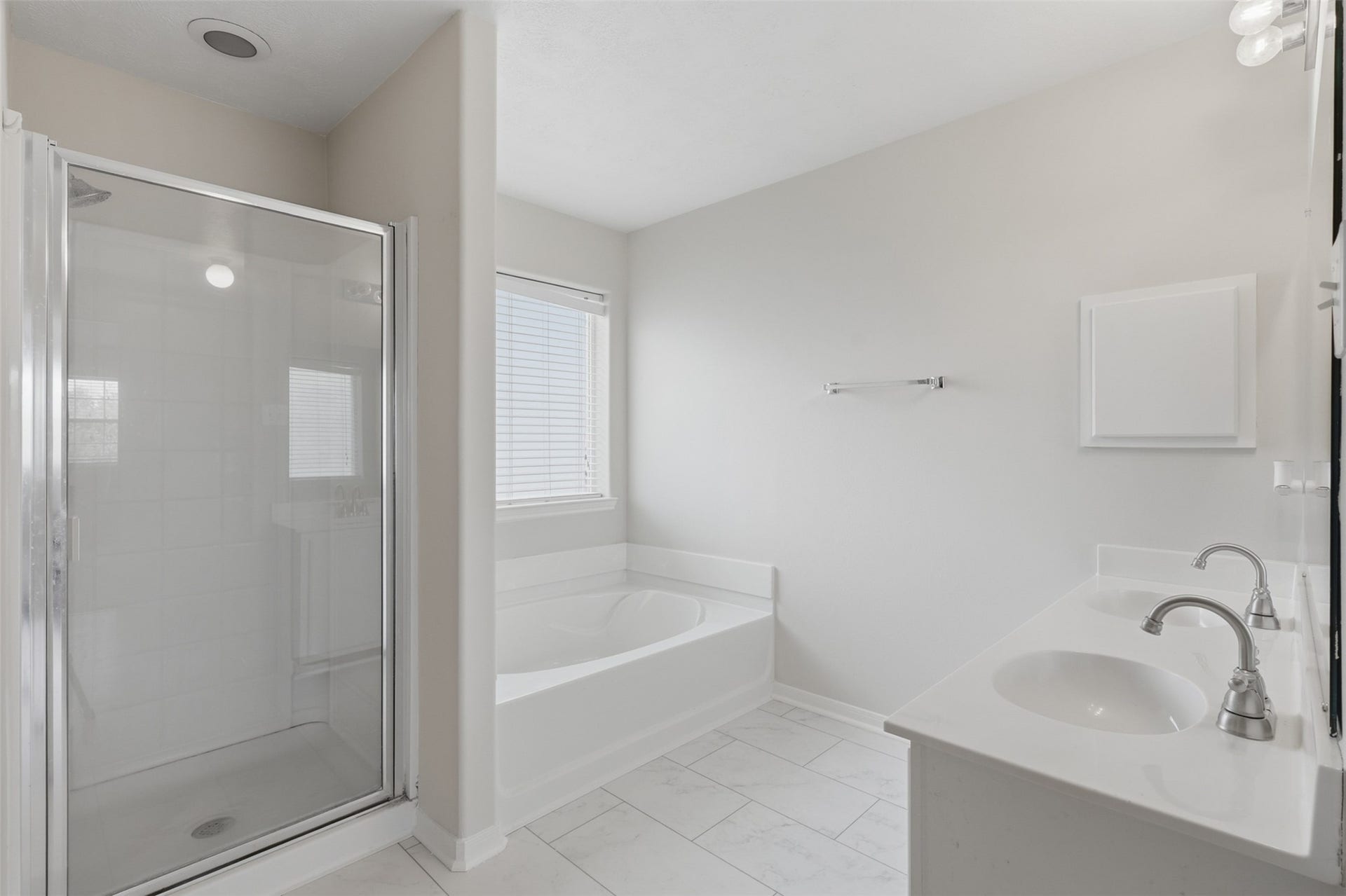 Continuing from the private entry landing, the primary en-suite opens into a bright, spacious bath featuring a double vanity, walk-in glass shower, deep soaking tub, and marble like tile flooring.