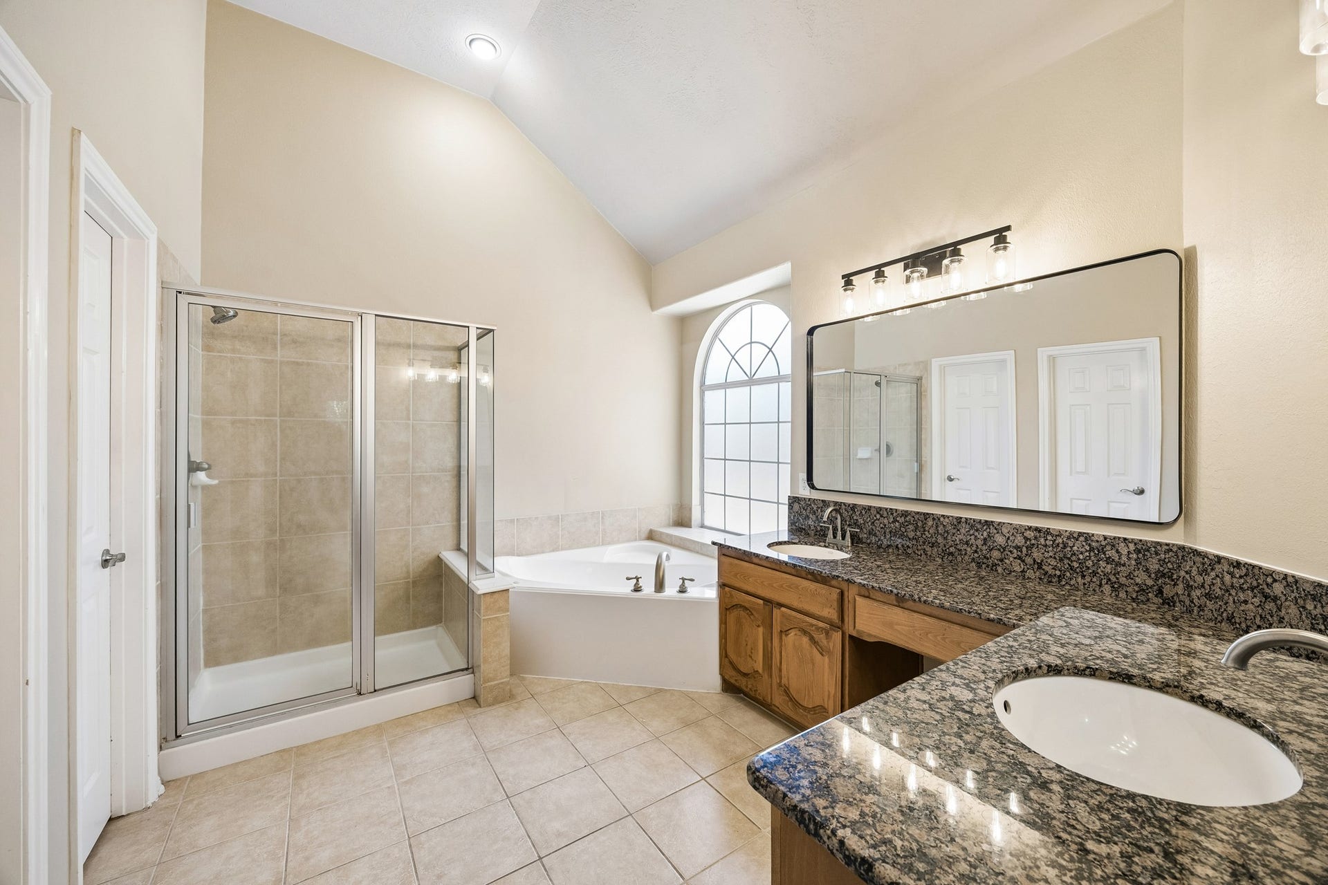 Spacious primary bath features dual vanities with generous counter space, a large soaking tub, separate glass-enclosed shower, abundant cabinetry, and natural light, creating a comfortable and functional private retreat.