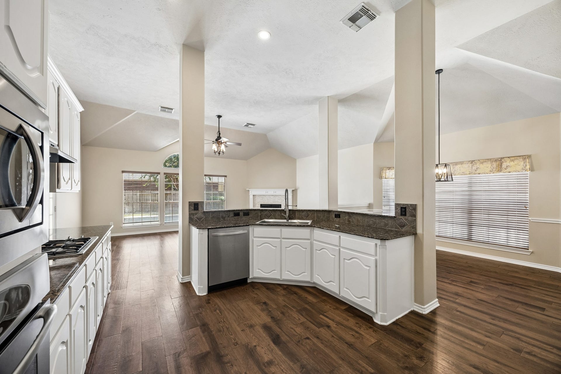 The heart of the home offers an open, functional kitchen with abundant white cabinetry, granite countertops, stainless steel appliances, and a large peninsula with bar seating, all opening seamlessly to the main living areas.