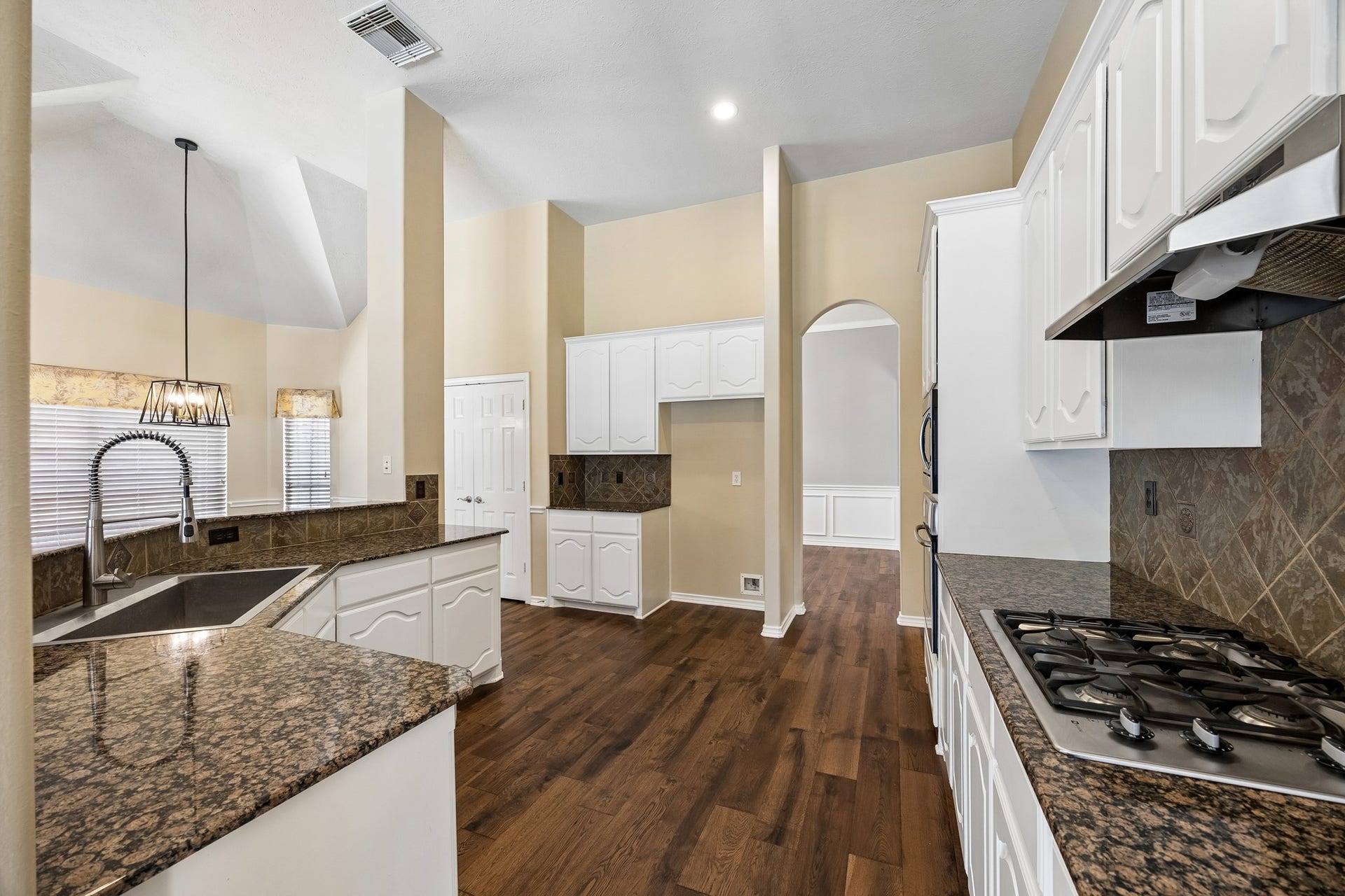 Bright, updated kitchen featuring crisp white cabinetry, granite countertops, stainless steel appliances, abundant storage, and engineered hardwood flooring, creating a fresh and inviting space for everyday living.