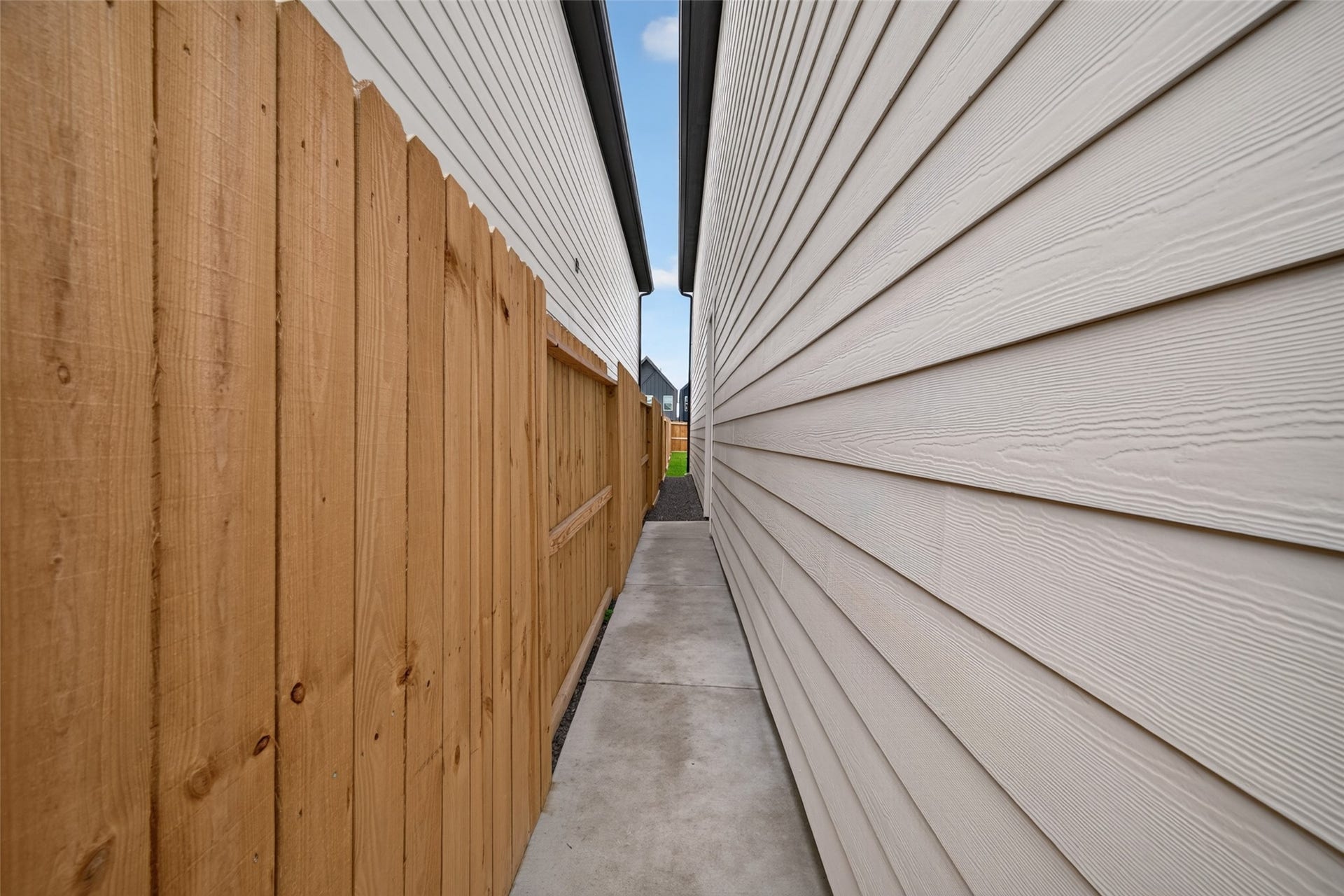 5915 Haight Street, #A, Houston, TX 77028 A narrow side pathway features a clean concrete walkway bordered by a wooden fence and the exterior siding of the house, leading to front side door.