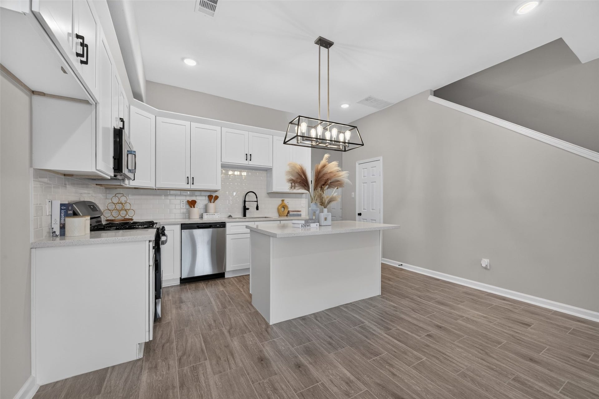 5915 Haight Street, #A, Houston, TX 77028 Modern kitchen with sleek white cabinetry, stainless steel appliances, and a spacious island under stylish pendant lighting.