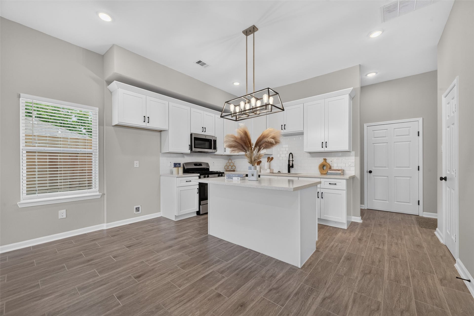 5915 Haight Street, #A, Houston, TX 77028 Chic and modern kitchen featuring sleek white cabinetry, a central island with elegant pendant lighting, and stylish wood-look flooring.
