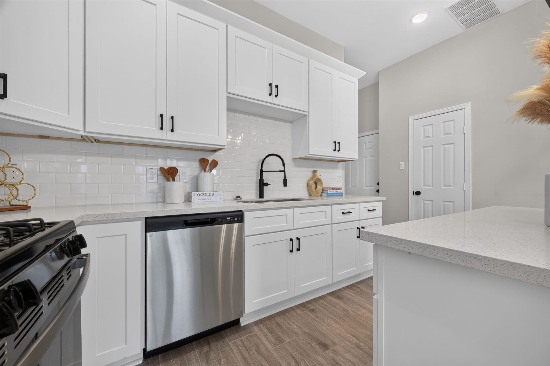 5915 Haight Street, #A, Houston, TX 77028 Modern kitchen with sleek white cabinetry, stainless steel appliances, and a stylish black faucet, complemented by a subway tile backsplash and wood-look flooring.
