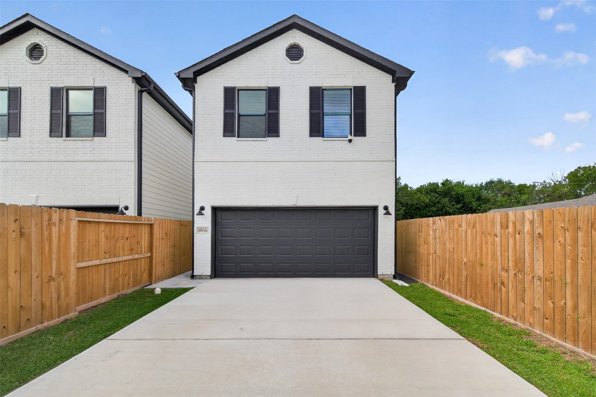 5915 Haight Street, #A, Houston, TX 77028 Modern two-story home with a sleek white exterior, dark shutters, and a spacious double garage, framed by a secure wooden fence and a well-maintained driveway.