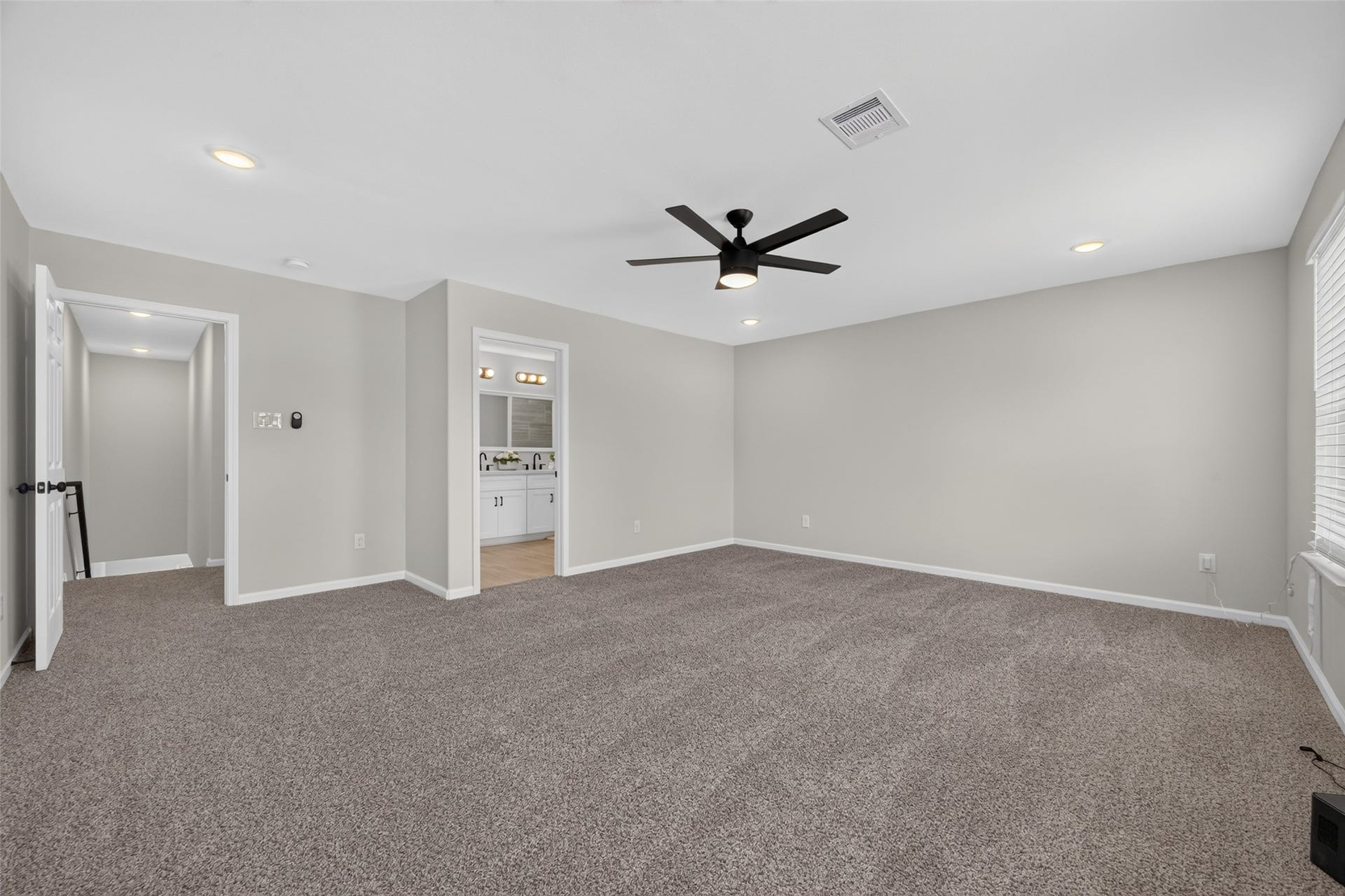 5915 Haight Street, #A, Houston, TX 77028 Spacious bedroom with plush carpeting, neutral walls, and a modern ceiling fan, leading to an ensuite bathroom with double vanity.