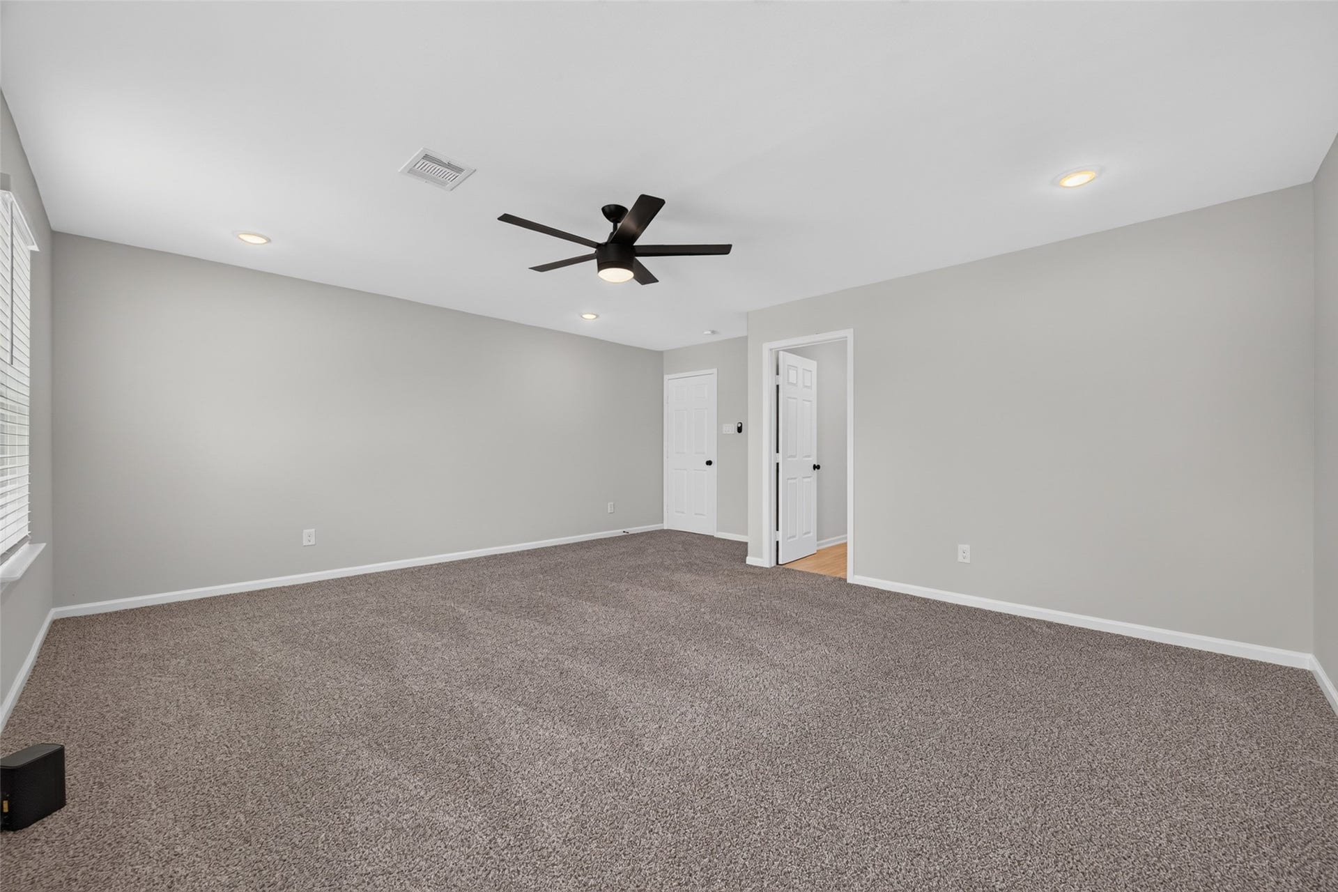 5915 Haight Street, #A, Houston, TX 77028 Spacious room with fresh neutral walls, plush carpeting, and a modern ceiling fan, offering ample natural light and a versatile layout.