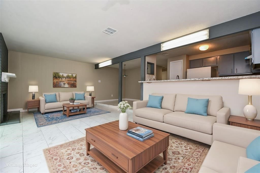 12569 Wellington Park Drive, Houston, TX 77072 This virtually staged photo showcases a spacious, open-concept living area with modern furnishings and neutral colors. It features a cozy seating arrangement, a fireplace, and a view into the kitchen, creating a warm and inviting atmosphere. Virtual staging was used.