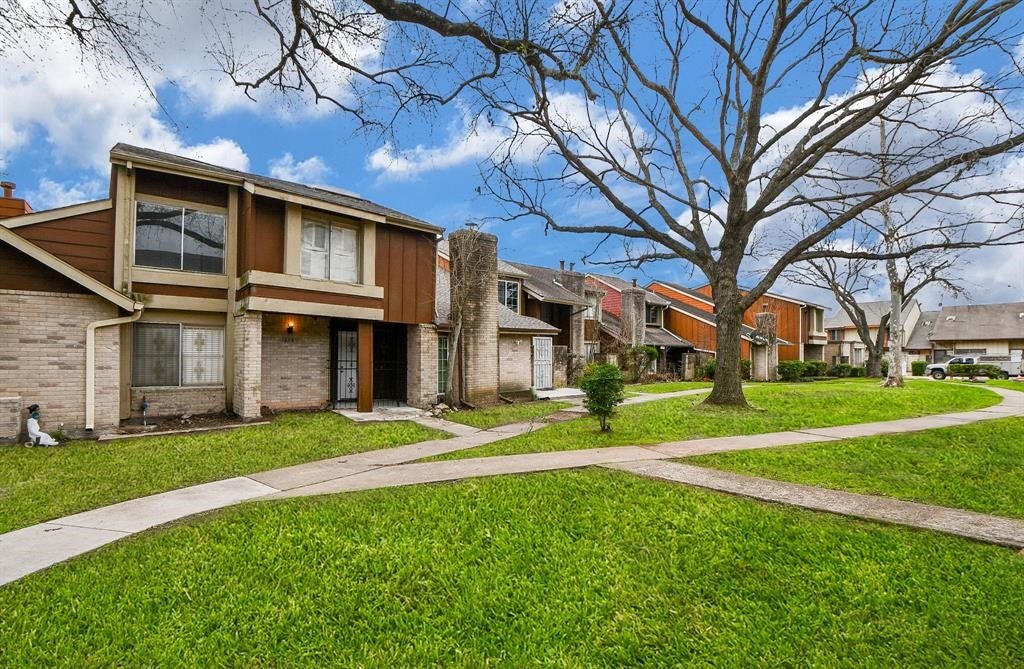 12569 Wellington Park Drive, Houston, TX 77072 This photo showcases a row of two-story townhouses featuring mixed brick and wood exteriors. The homes are set along a curved, tree-lined path with well-maintained lawns, providing a welcoming neighborhood atmosphere.