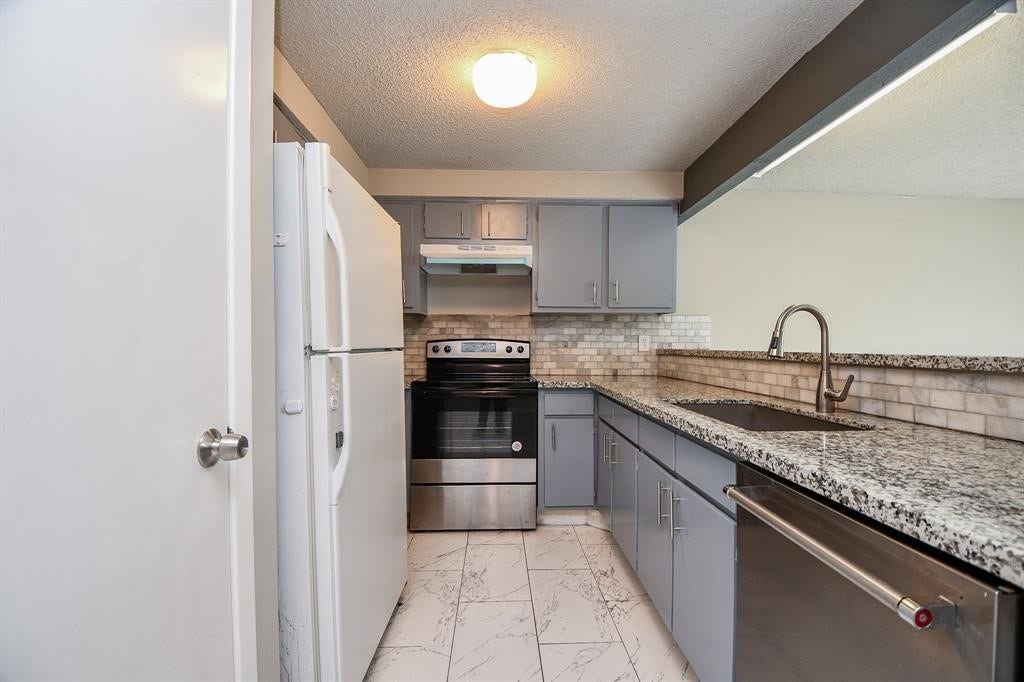 12569 Wellington Park Drive, Houston, TX 77072 Modern kitchen with sleek granite countertops, stainless steel appliances, and light gray cabinetry. The space features a tiled backsplash and a clean, bright atmosphere.