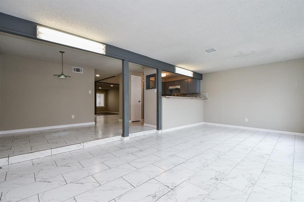 12569 Wellington Park Drive, Houston, TX 77072 Spacious room with light-colored tile flooring and neutral walls, featuring an open layout that connects to a kitchen with a breakfast bar. Recessed lighting and a large window provide ample natural light.
